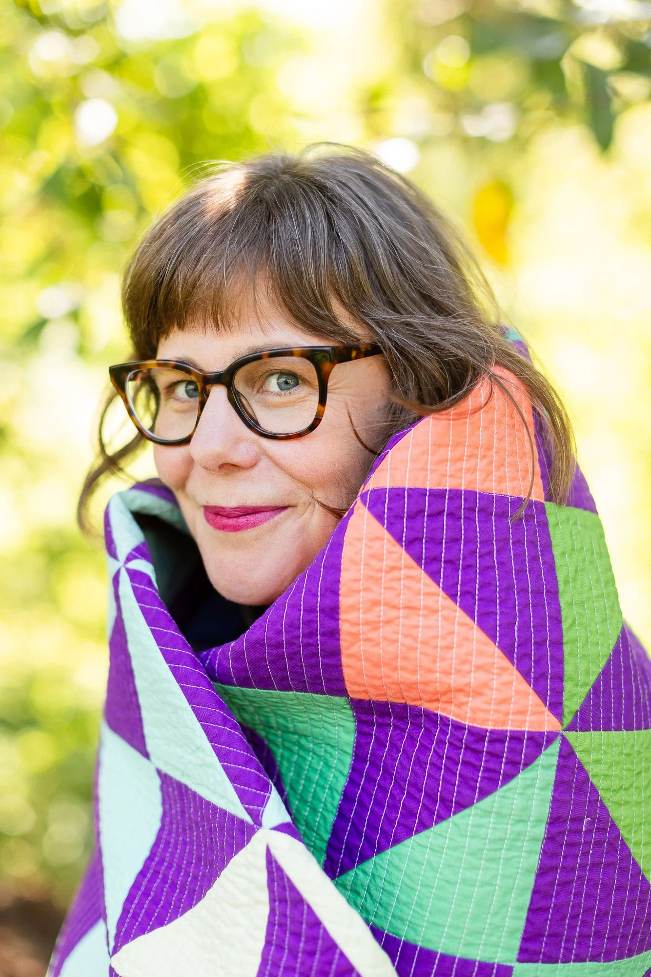 woman wearing glasses smiling at camera wrapped in a quilt.