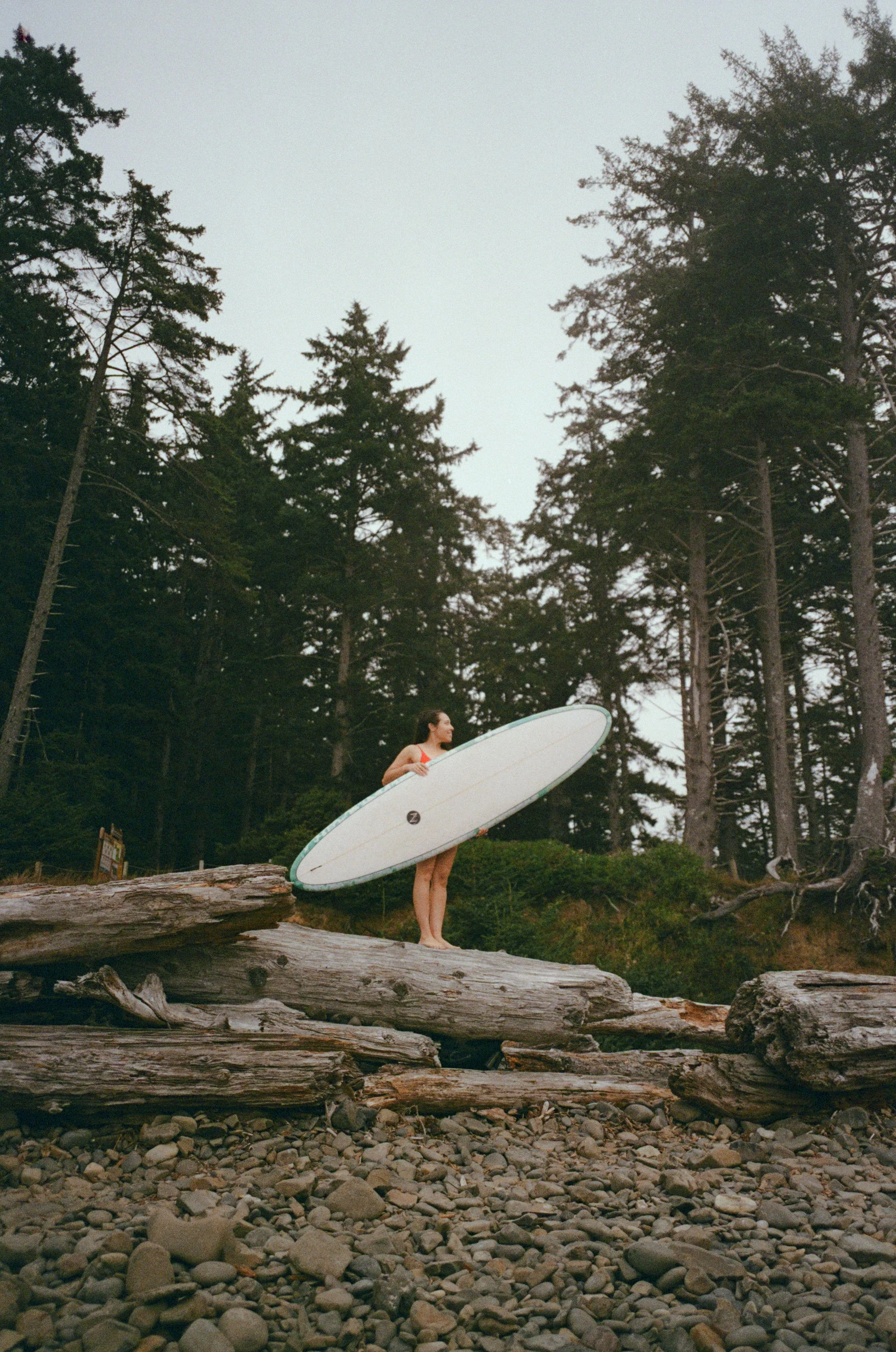woman holding surfboard standing on a log.
