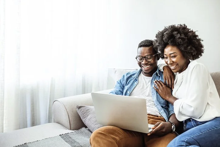 Couple smiling at laptop on sofa during online therapy in Chicago, Illinois.