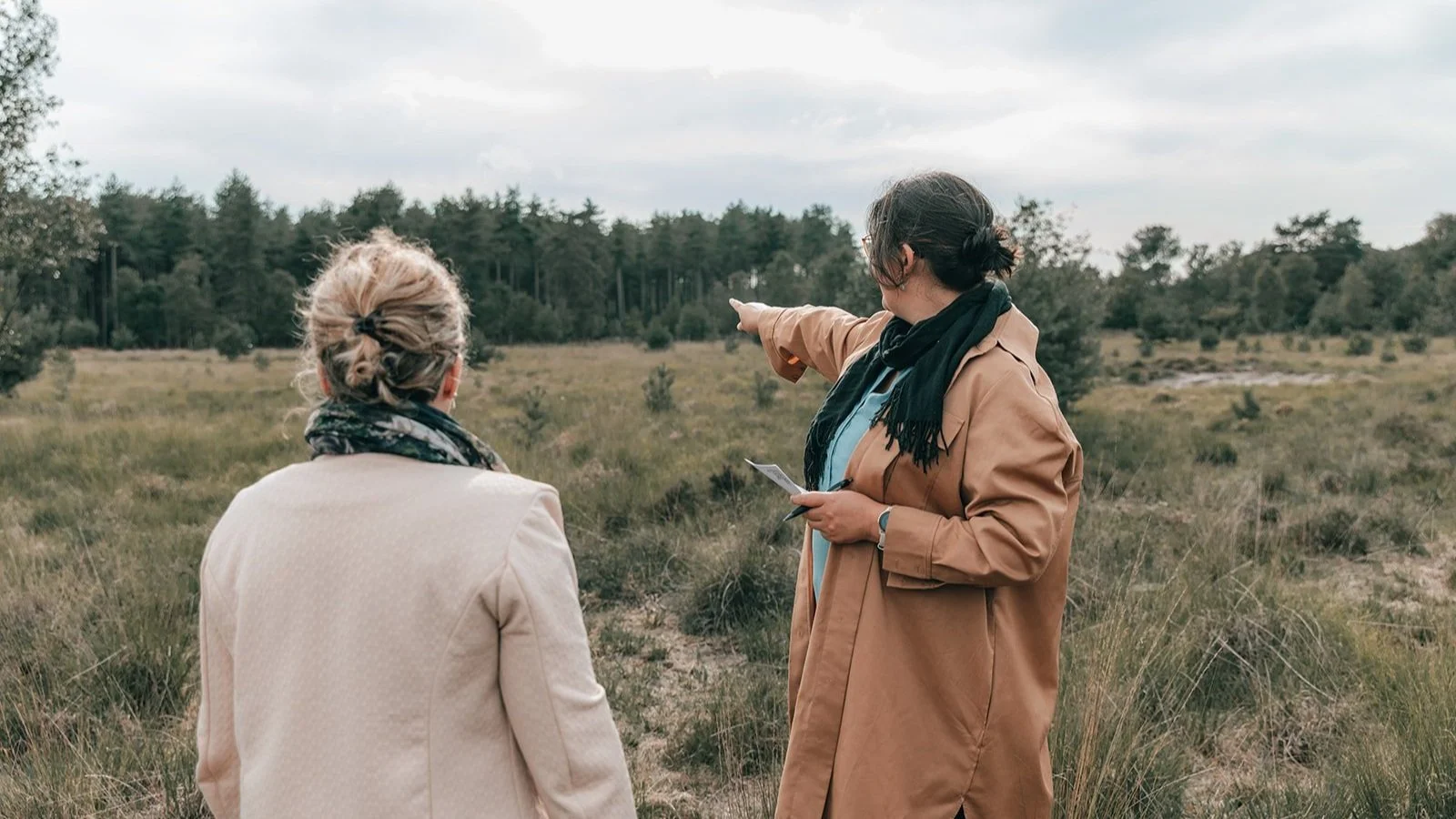 Twee vrouwen in een grasland bespreken of wijzen op iets in de verte tijdens een wandeling.