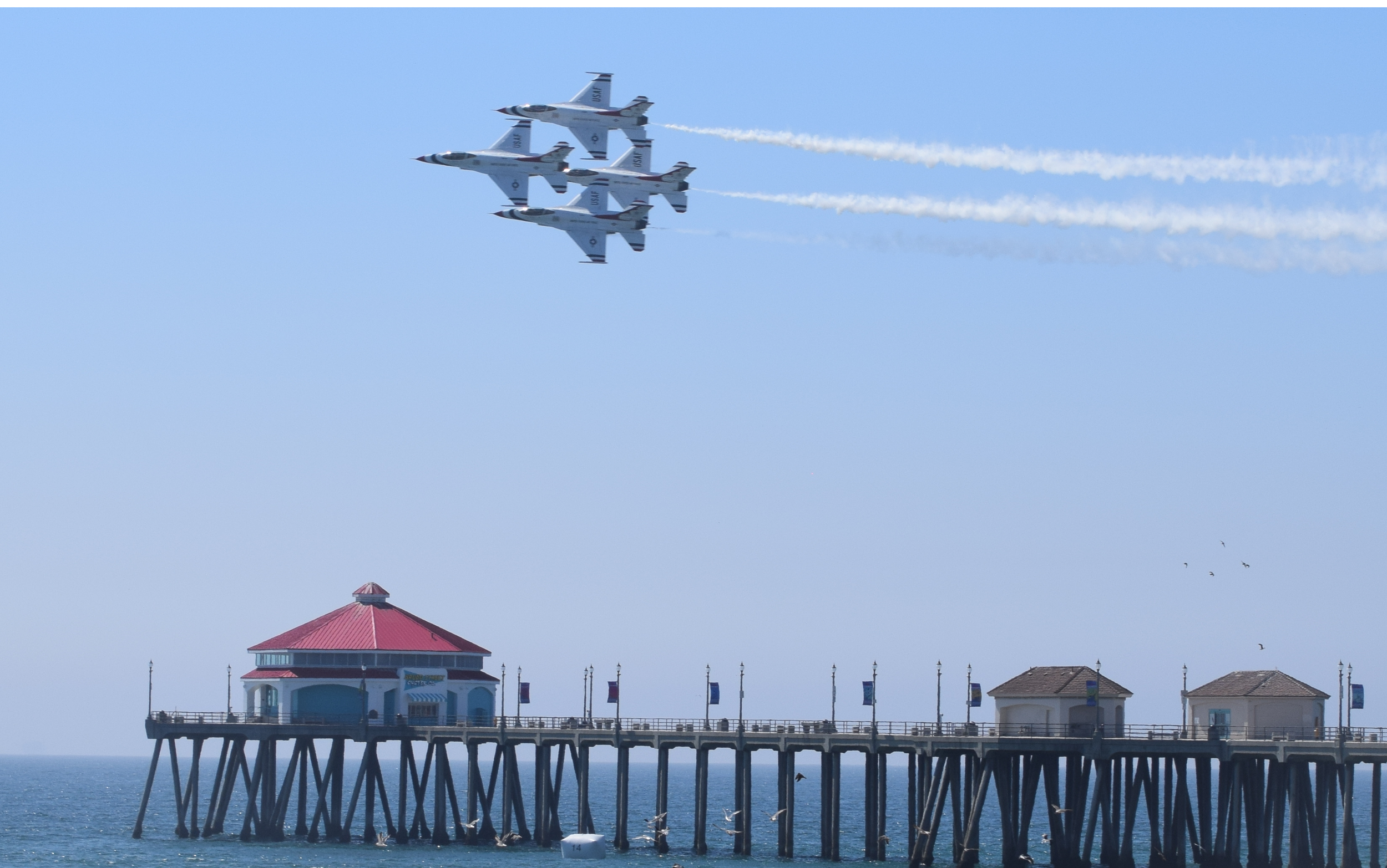 United States Air Force Thunderbirds flying diamond formation over the Huntington Beach pier.