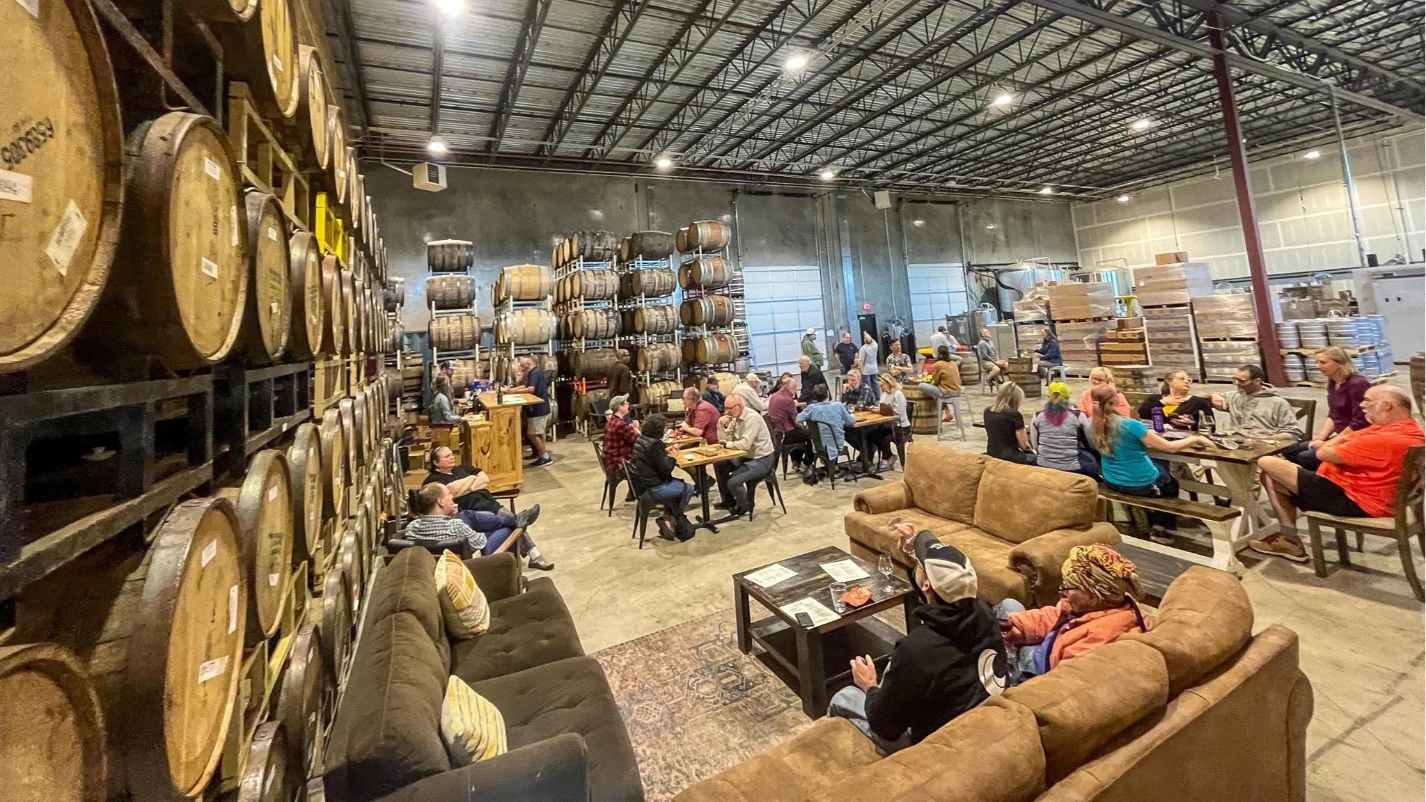 Group of people sitting in a warehouse with wooden barrels.