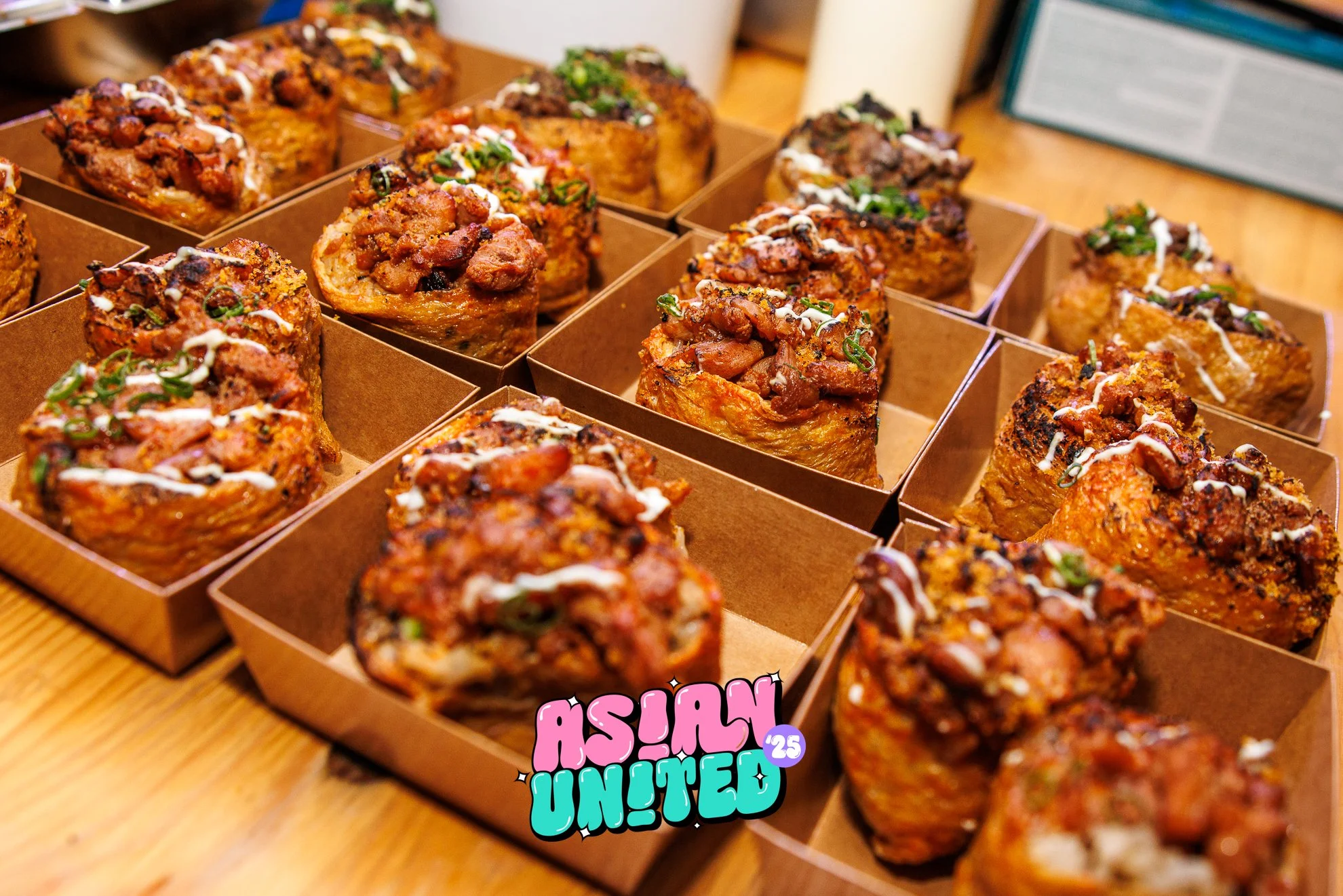 Mehrere knusprige Muffins mit Fleisch, Käse und Frühlingszwiebeln, in braunen Pappboxen, auf einem Holztisch.