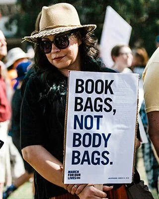 woman holding sign that reads - book bags, not body bags