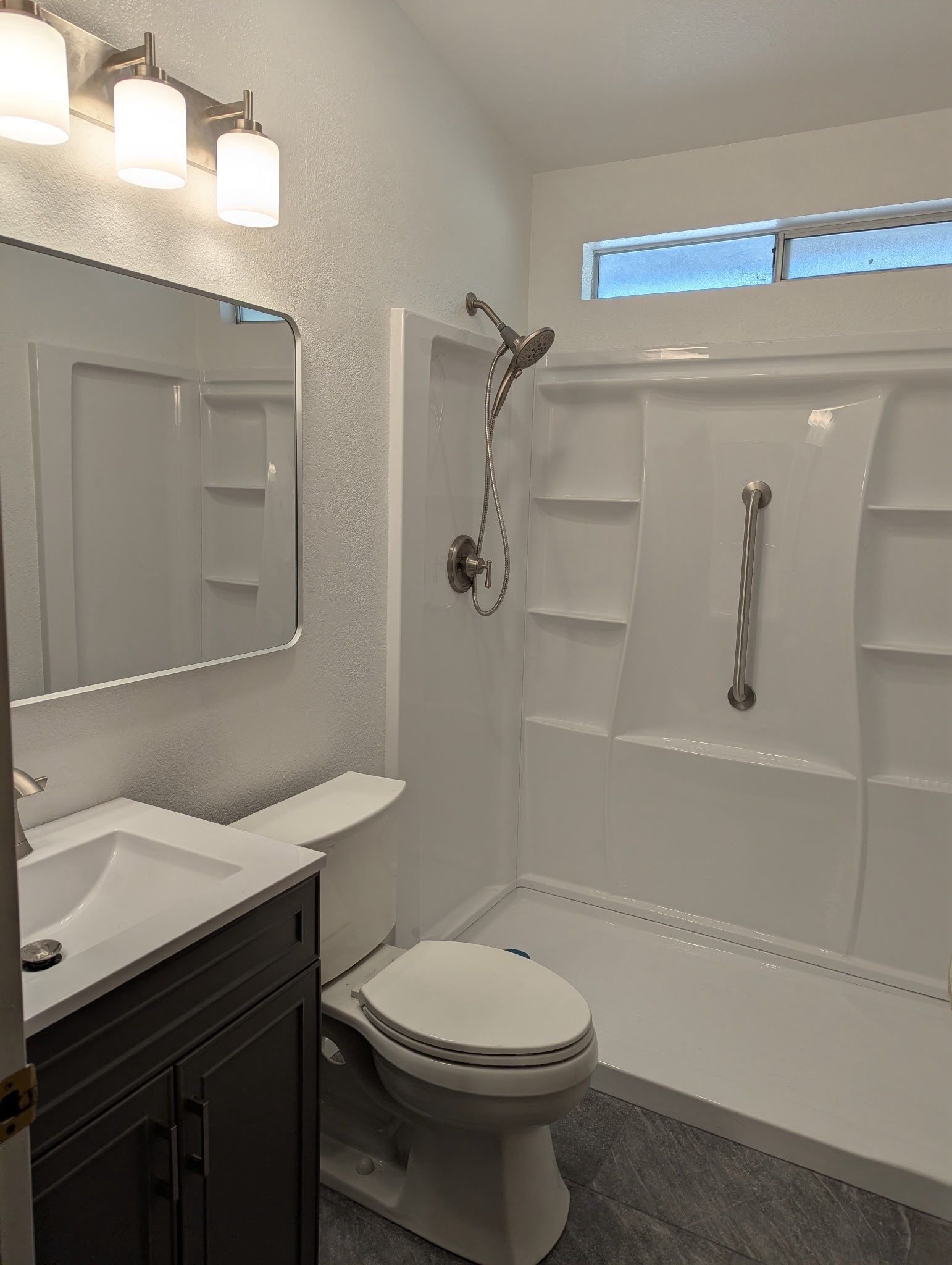 New white walk-in shower with grab bar and gray vanity in a remodeled Rio Linda bathroom