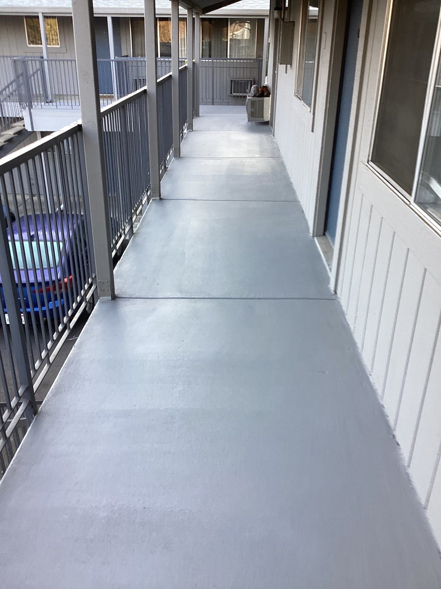 Repaired second-story apartment walkway with new coated surface and metal railings in Sacramento, CA