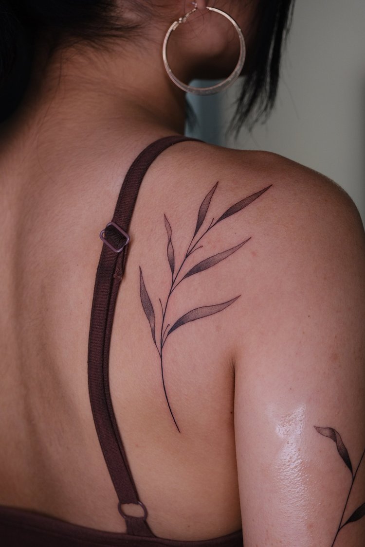 Fine line botanical sprig tattoo on a shoulder by Eli