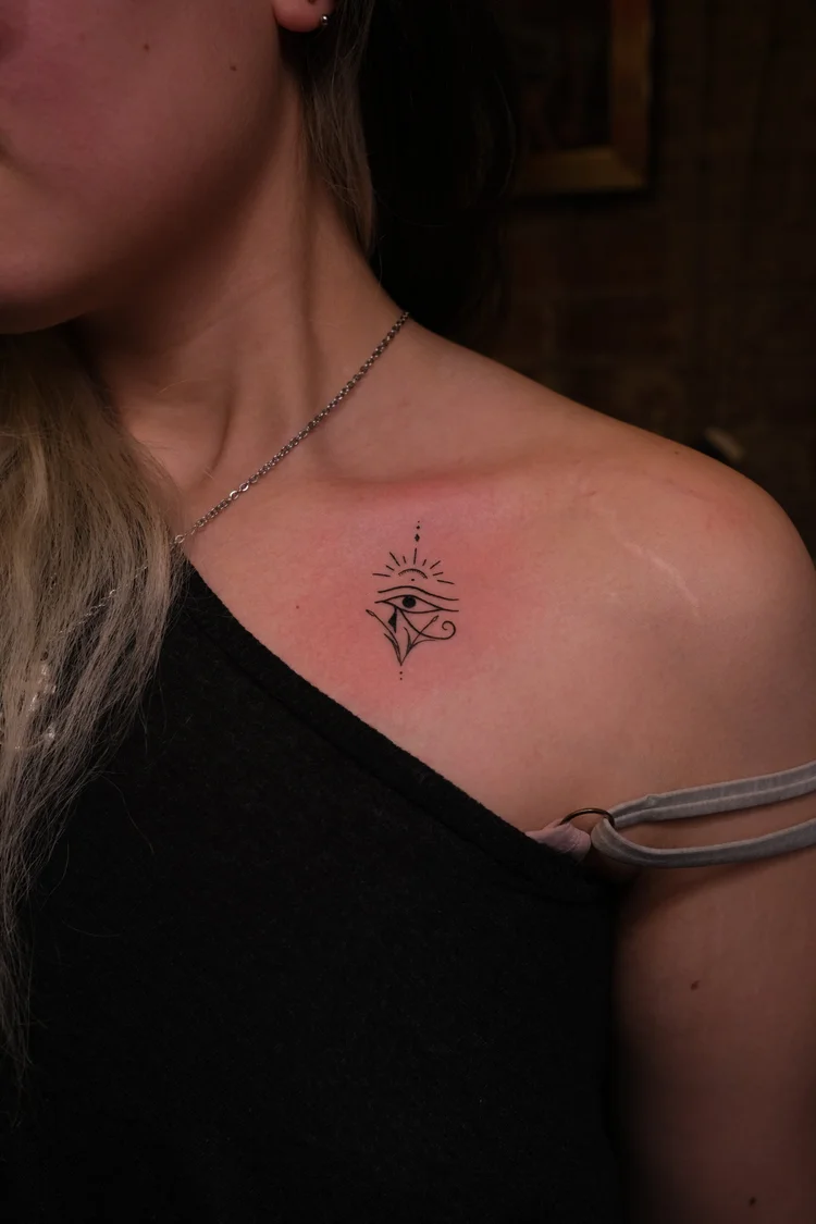 Fine line eye and sun ray tattoo on the upper chest by Eli