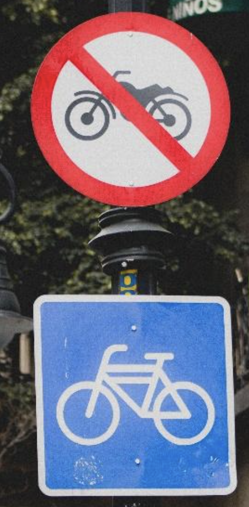 A round sign with a motorcycle silhouette and a red line across it indicating motorcycles are not allowed. Underneath, there is a square blue sign with a bicycle silhouette indicating that they are allowed.