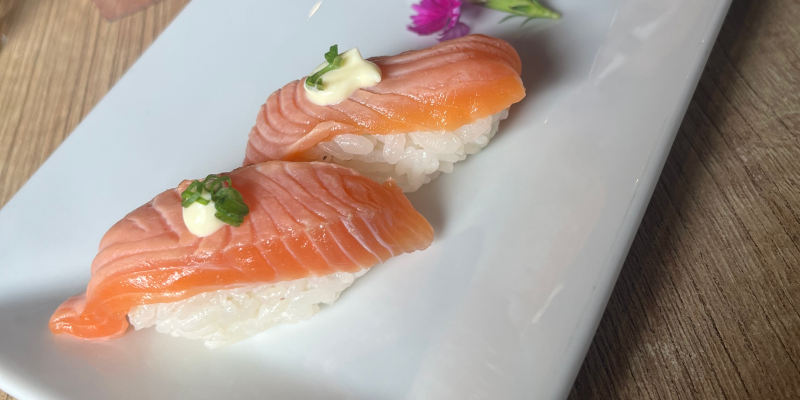 Dos piezas de sushi de salmón servidas sobre un plato blanco rectangular, acompañadas de una salsa cremosa debajo del pescado.