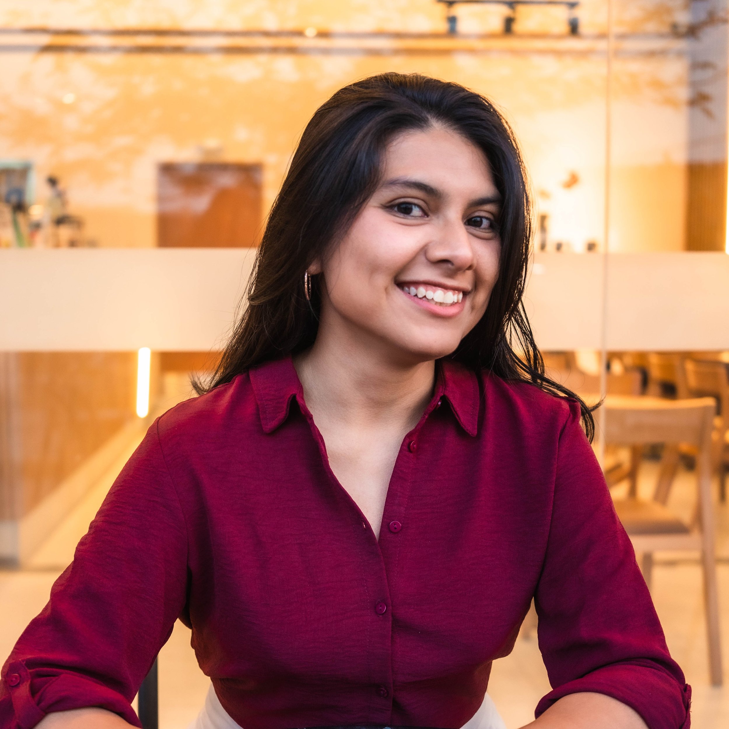 Karien mirando hacia la pantalla con una camisa color vino de botones.