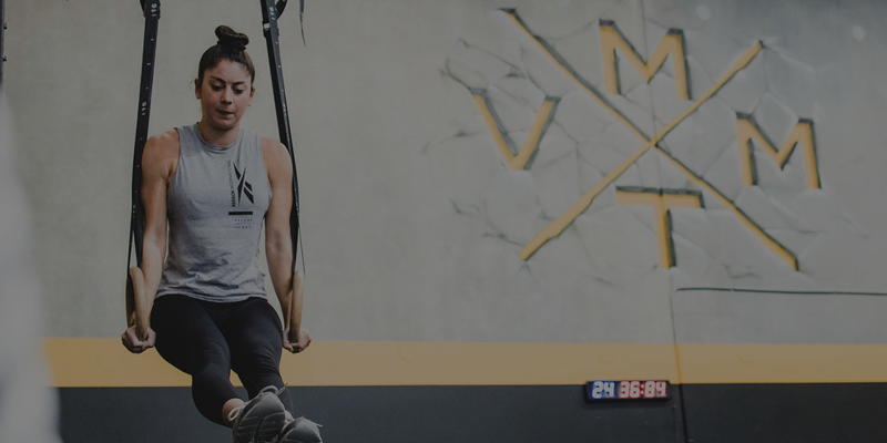 A woman exercising on a weighted jump rope in a gym with a logo on the wall and a digital timer.