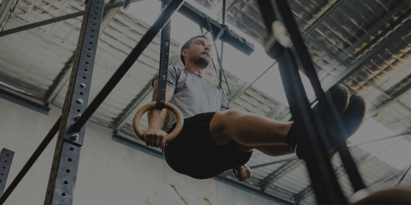Man performing ring muscle-up exercise on gymnastic rings in a gym setting.