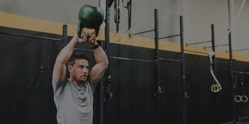 Man lifting a kettlebell overhead in a gym.