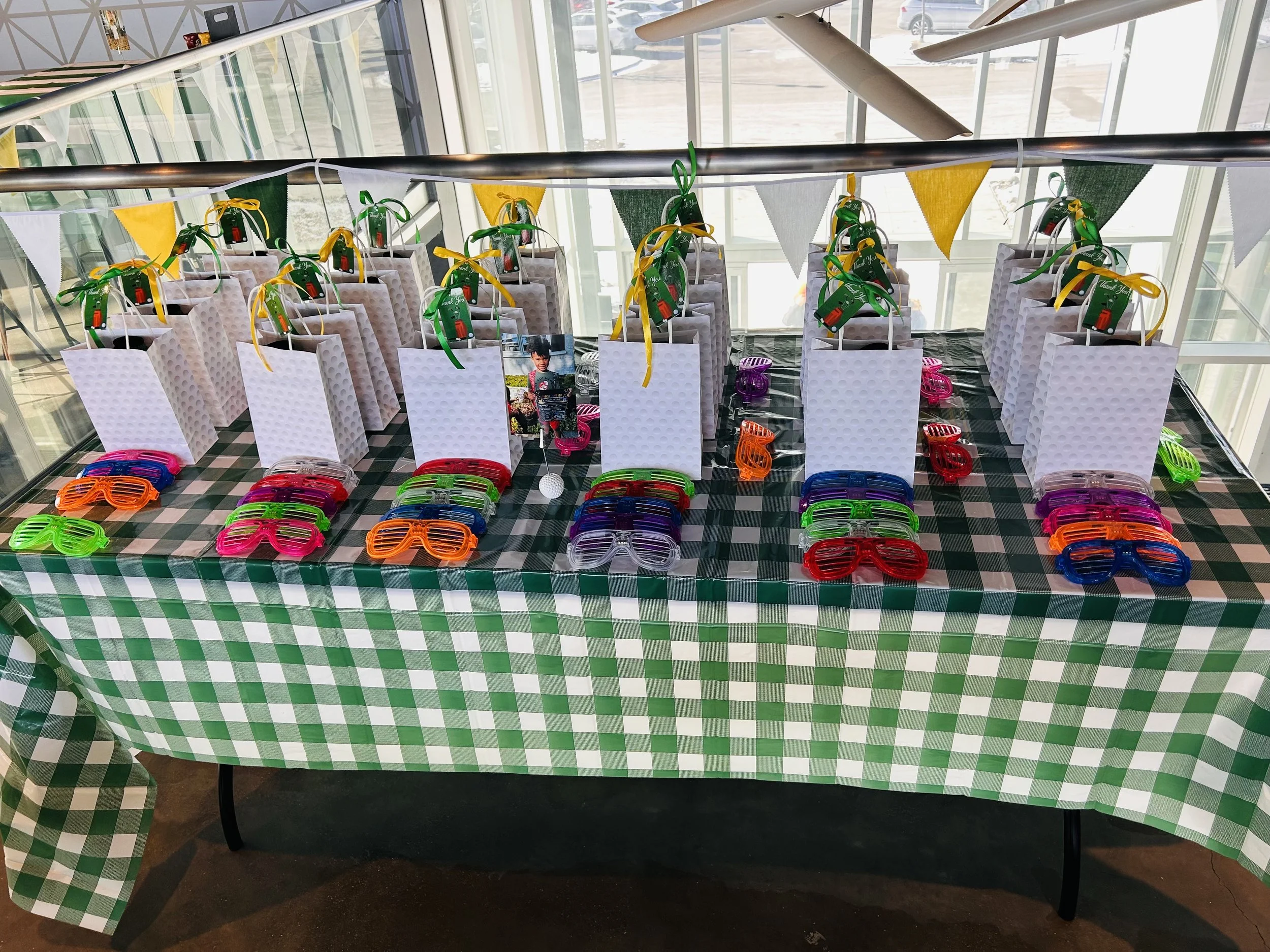 gift table for kids birthday party. golf themed birthday party. green and white checkered table cloth with fun gifts. flags to decorate the golf themed birthday party and gift or goodie bags for the kids to take home. 