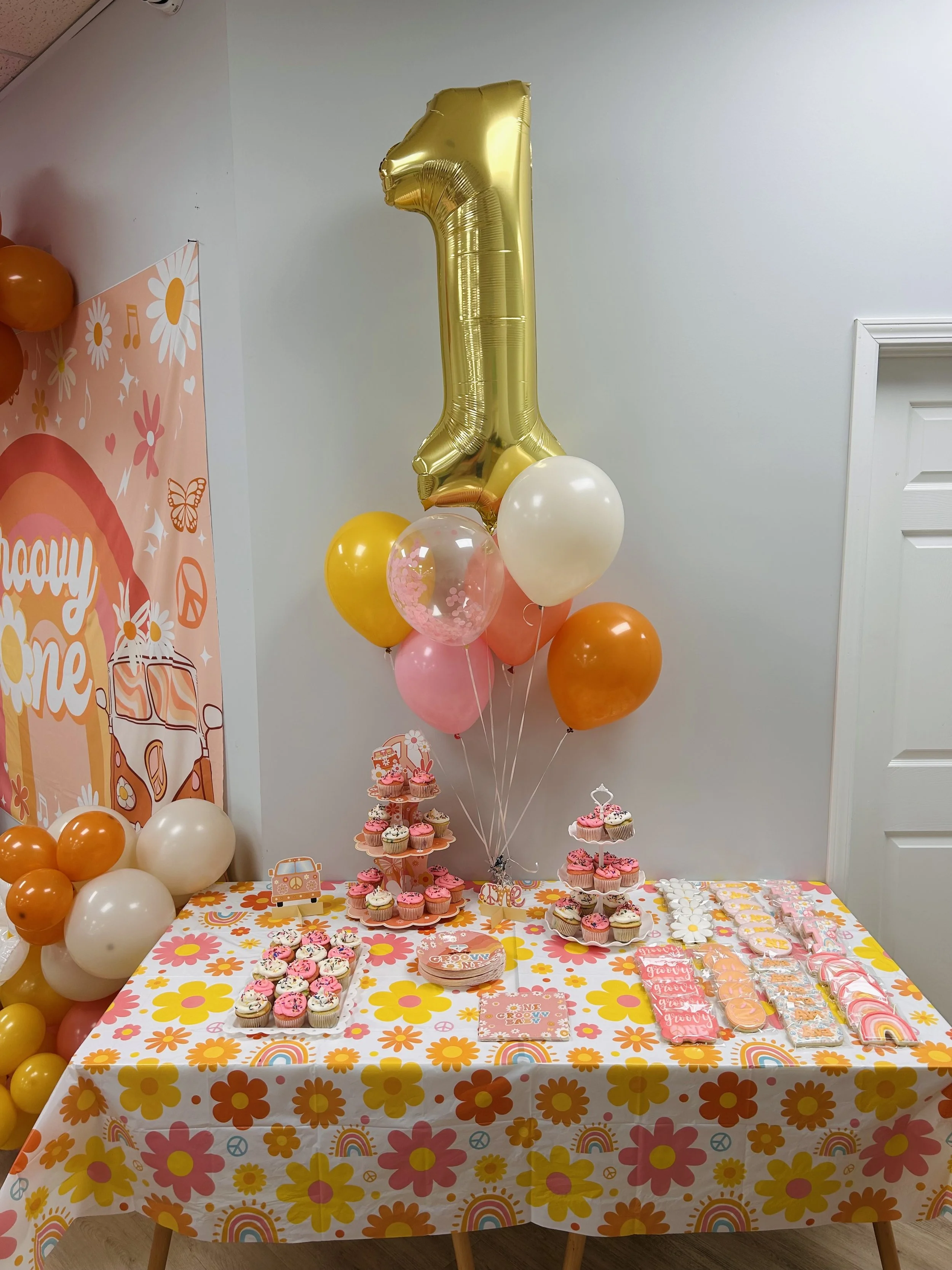 dessert table for babys first birthday party. dessert table filled with custom cupcakes and cookies. balloons with colors to match the theme of the birthday party and a big 1 balloon for decor. 