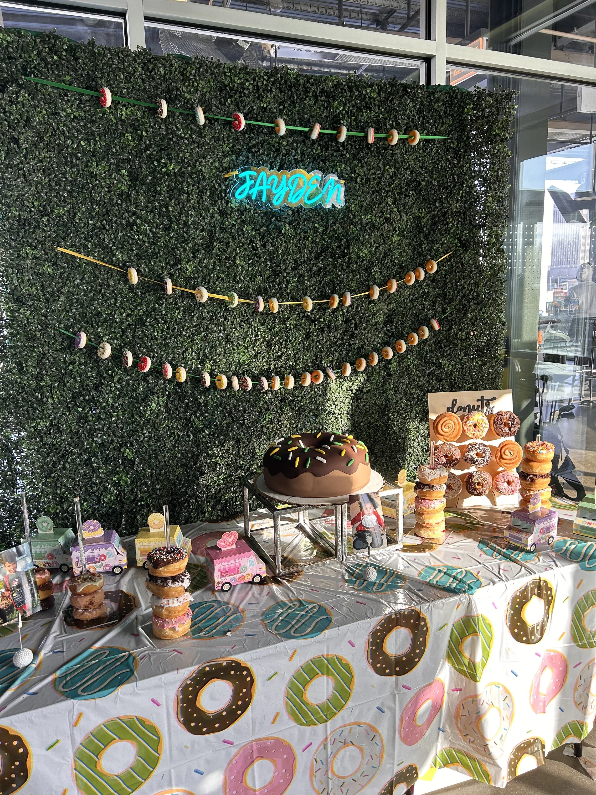 dessert table. donut themed dessert table. green wall with donut string and LED name sign for birthday boys. donut stands and a very large donut cake to fit the theme for this golf themed birthday party.  