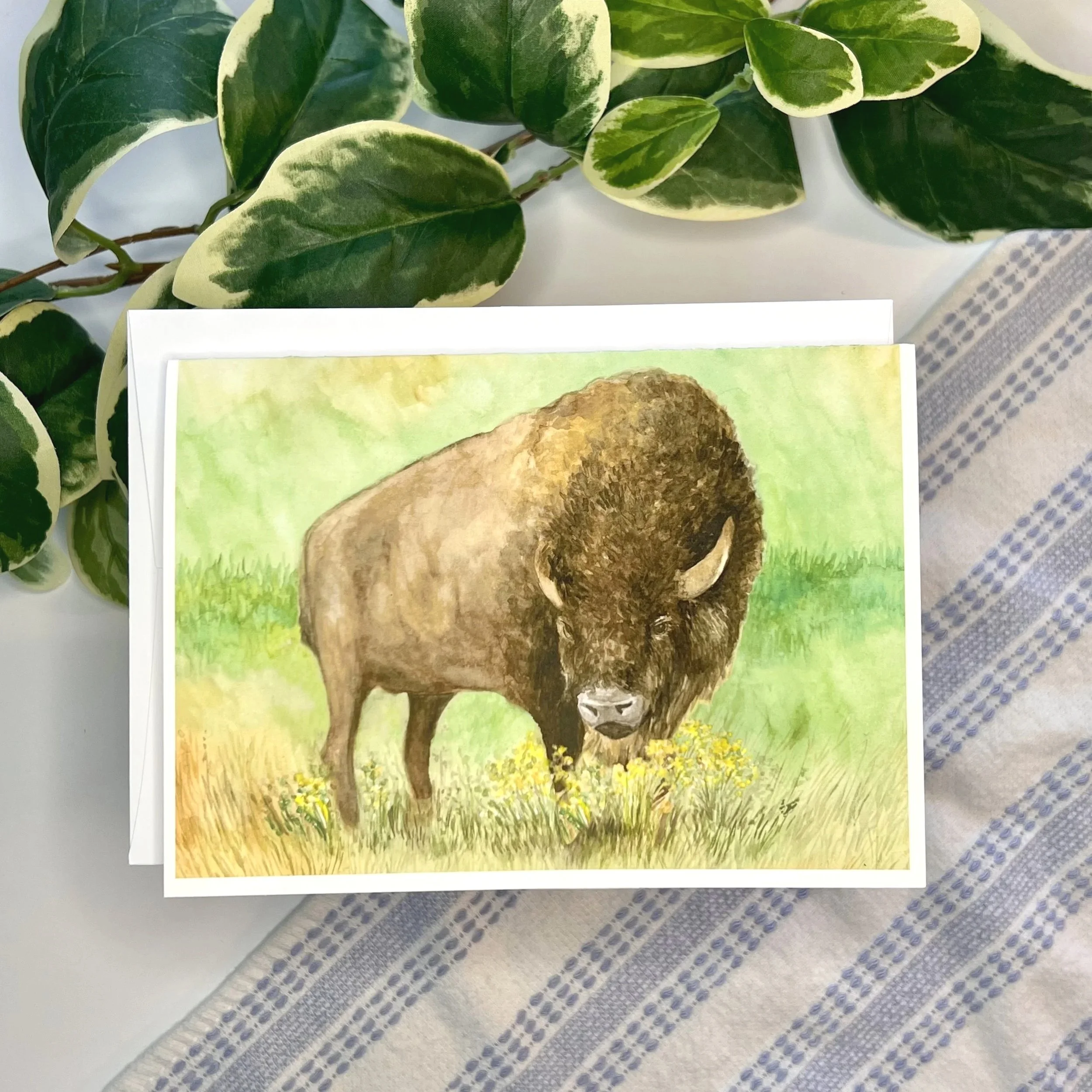 Blank greeting card featuring a watercolor painting of a proud buffalo grazing in a flowery field.