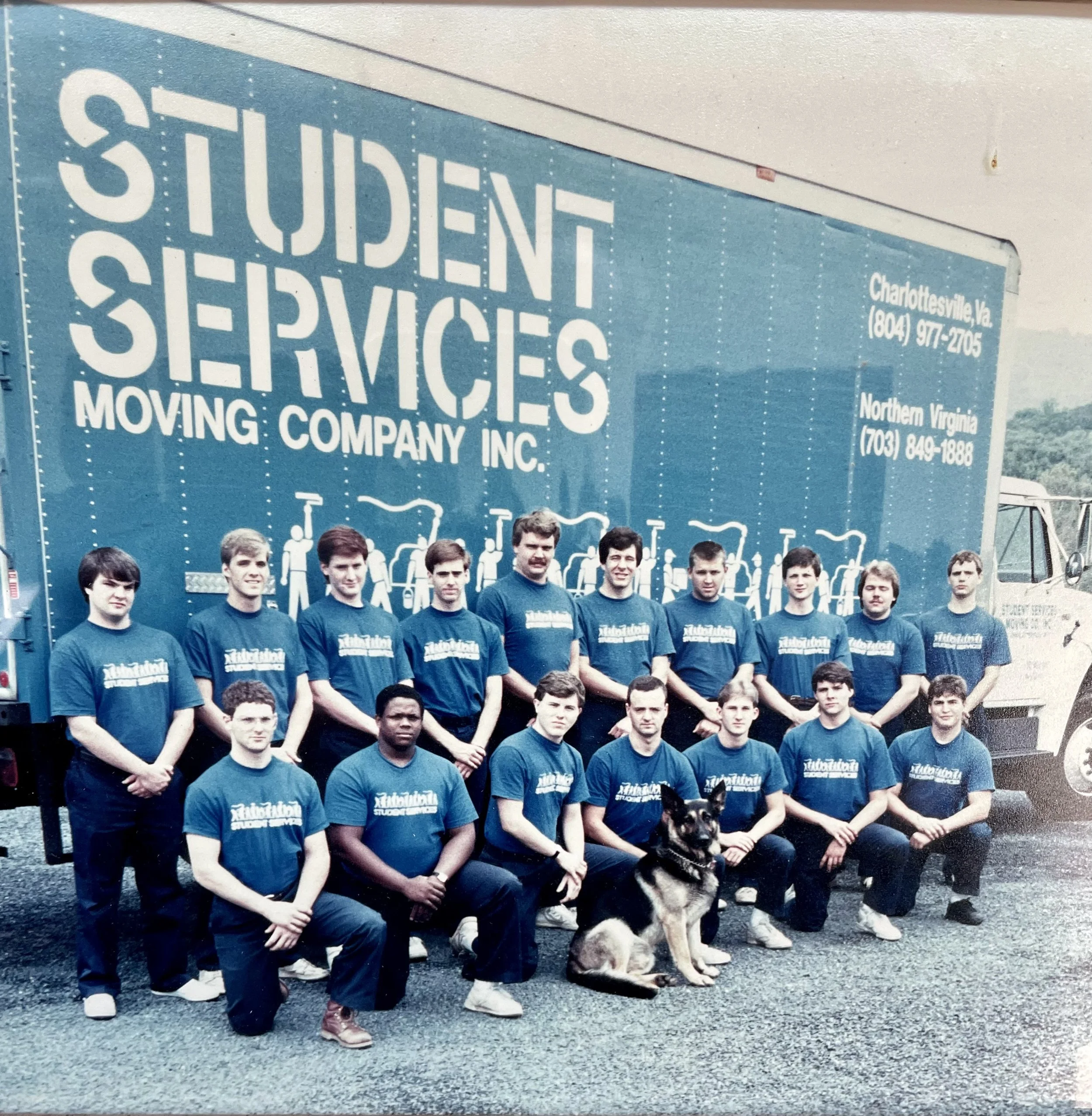 Group photo of student service members from Moving Company Inc., with a large moving truck in the background, featuring the company's name and two locations in Virginia.