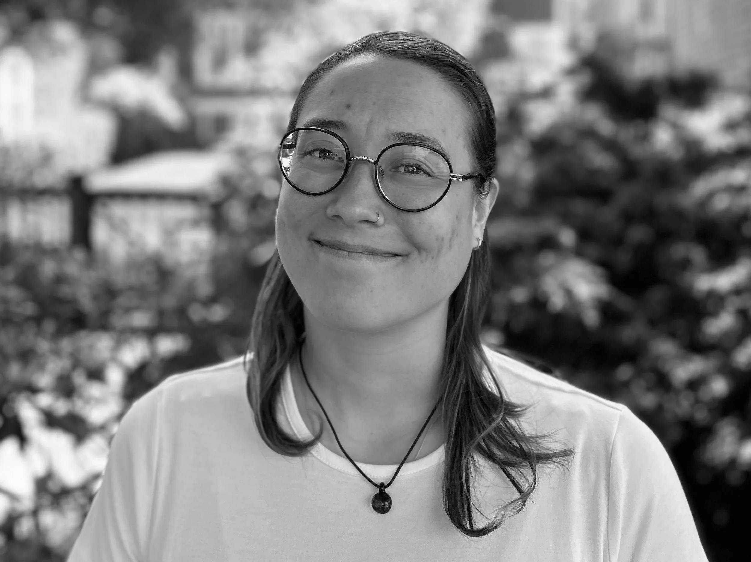 A woman with glasses smiling outdoors in black and white.