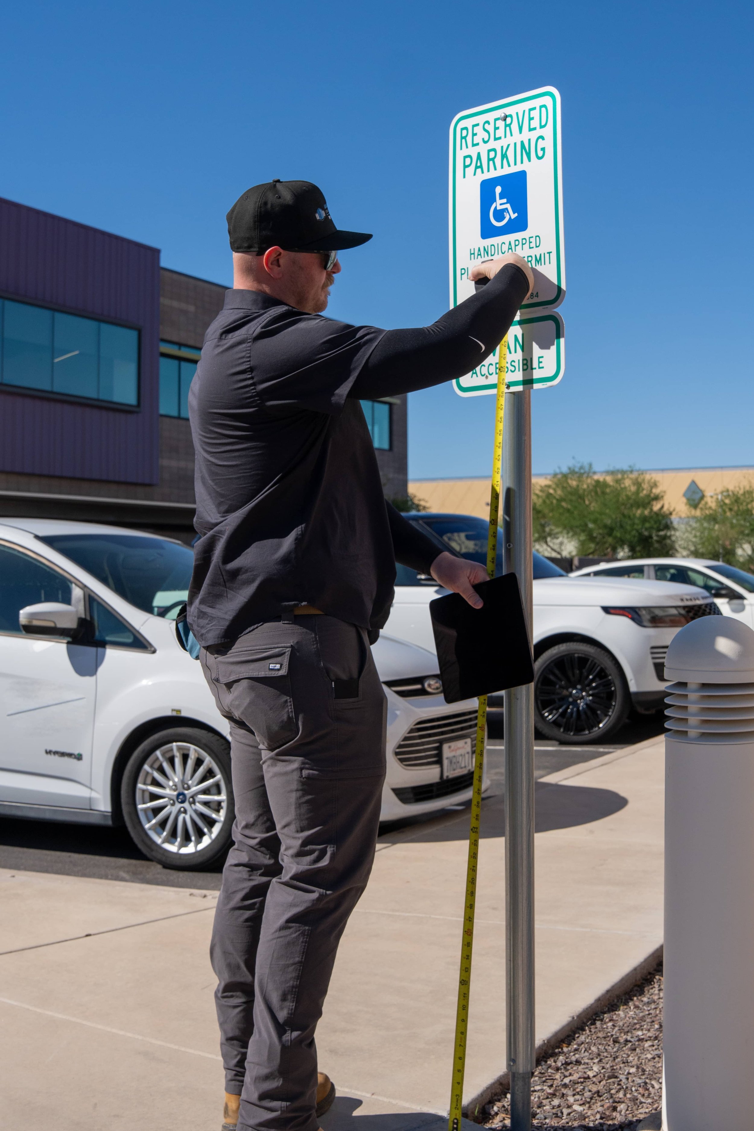 Man adjusting a parking sign that reads reserved parking for handicapped on a bright sunny day in a parking lot.