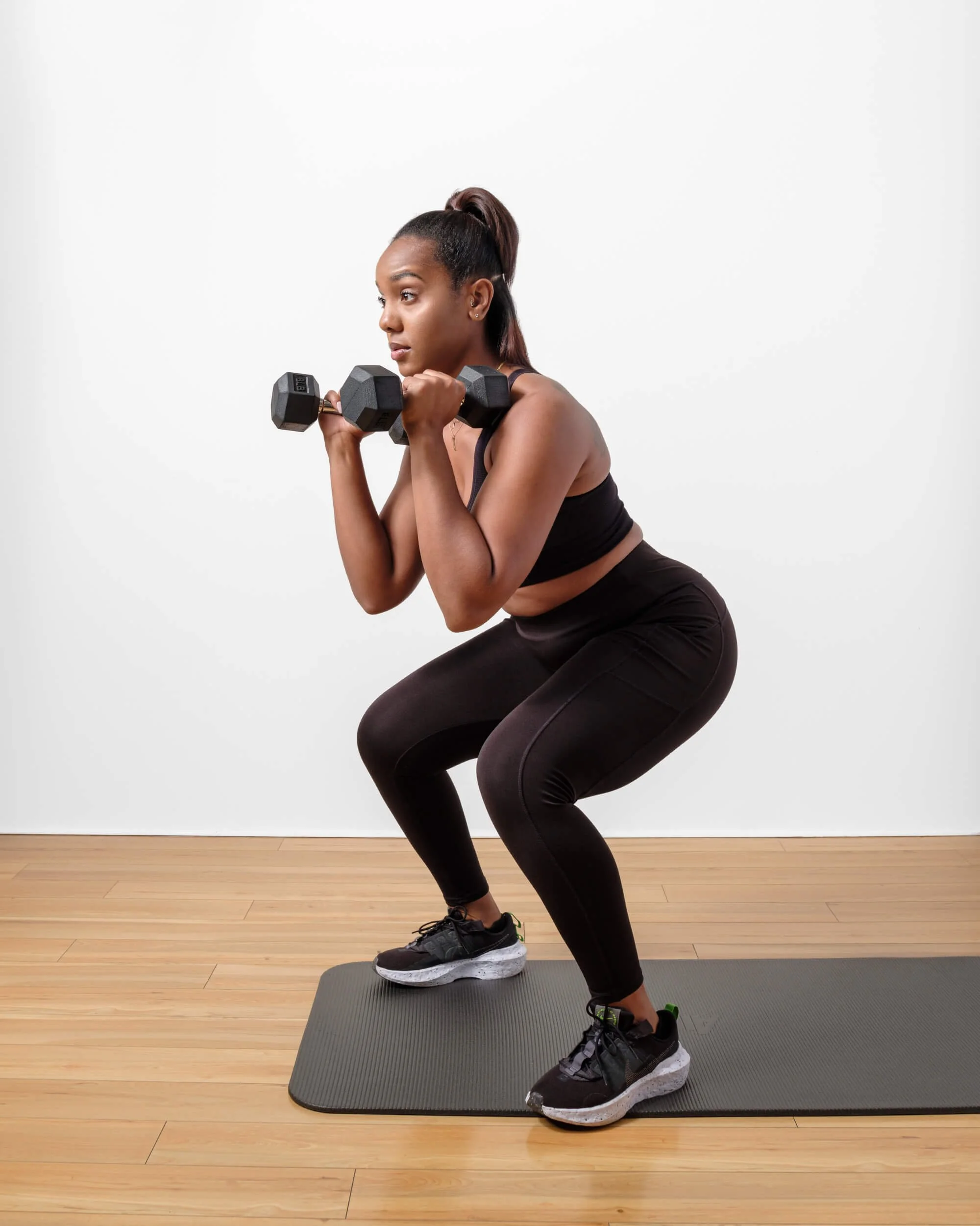 Young female in workout attire doing squats with dumbells