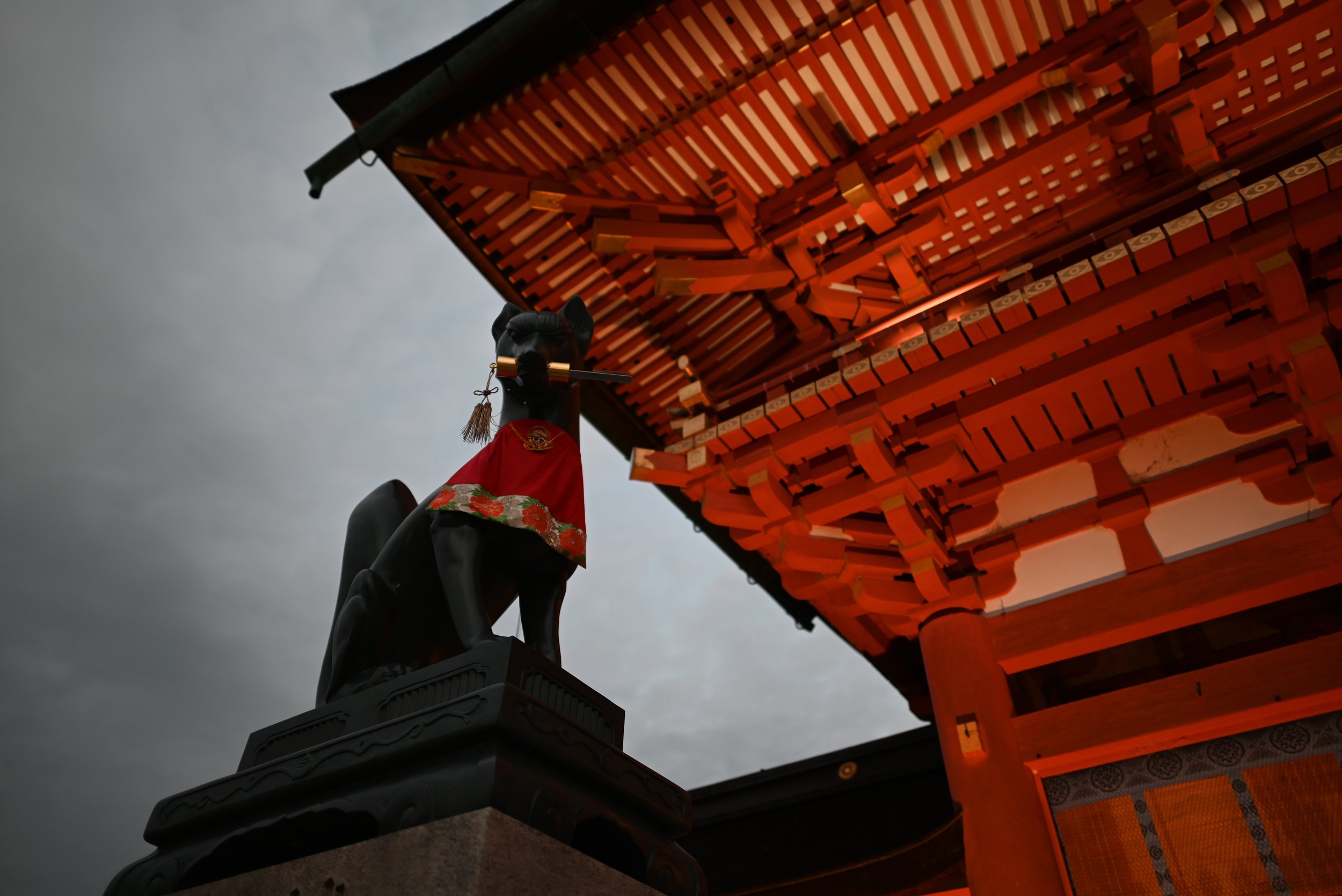 In Japanese mythology, foxes, or kitsune, are legendary creatures with paranormal abilities. This is a fox statue at the entrance to Fushimi Inari, a shrine with thousands of bright orange tori gates.