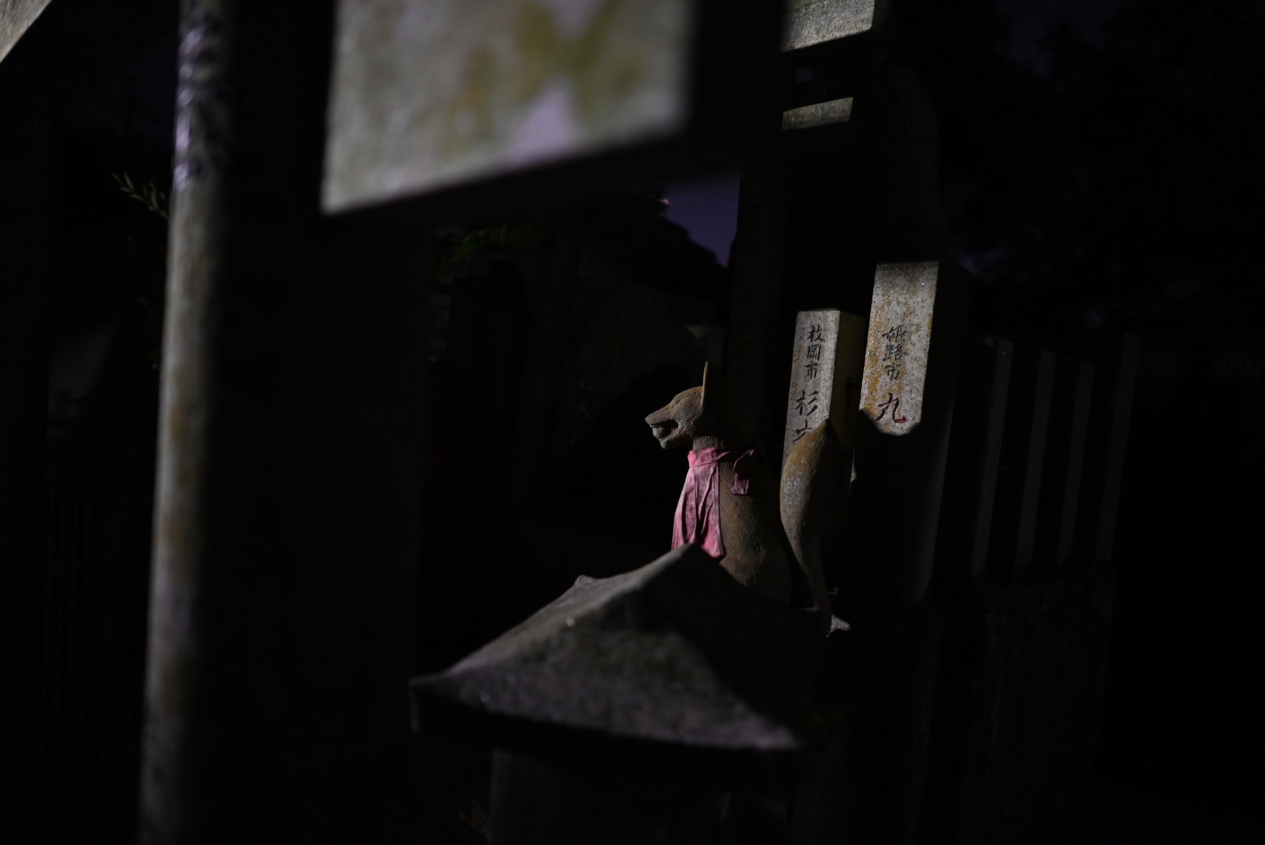A fox statue amongst stone tori gates at a shrine near the Fushimi Inari gates of Kyoto.