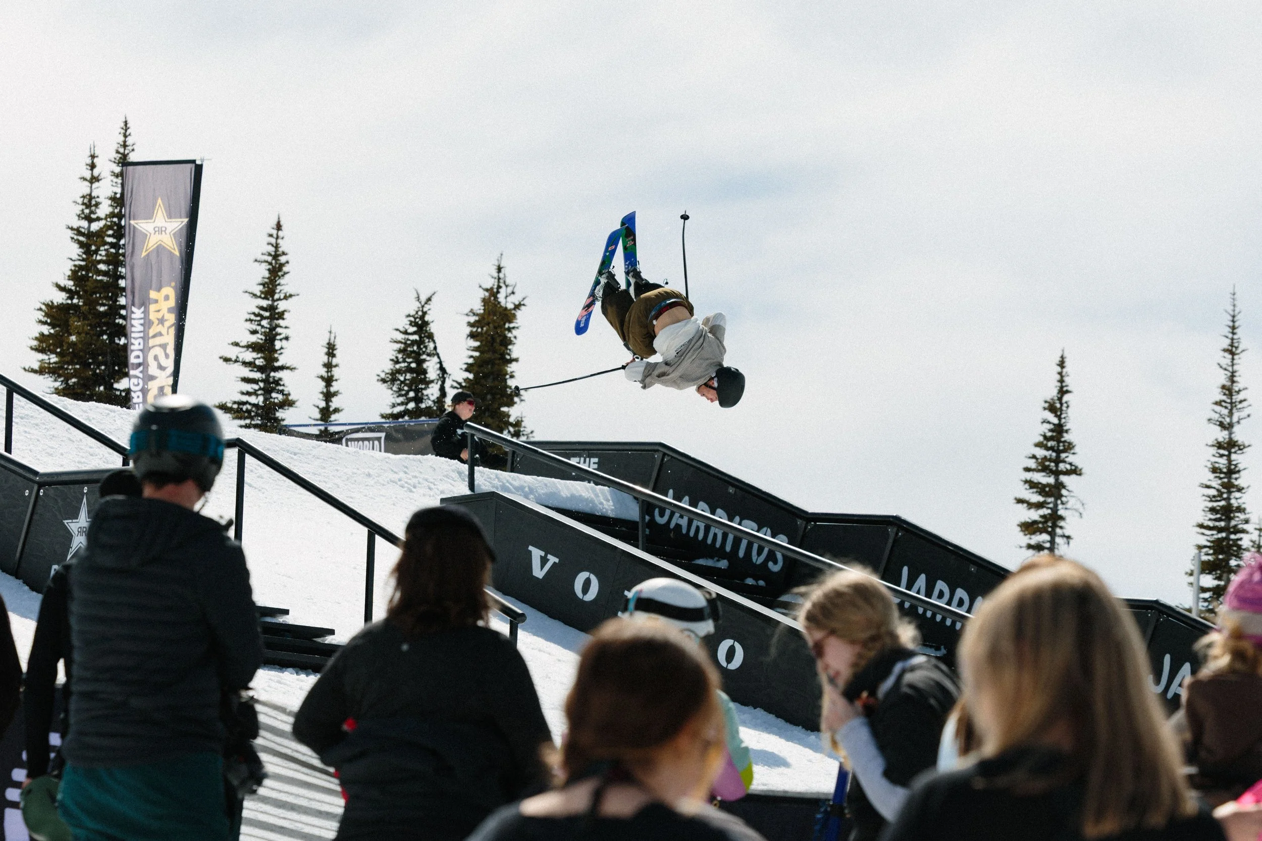 A skier performing an upside-down stunt on a ramp during a snowboarding event, with spectators watching.