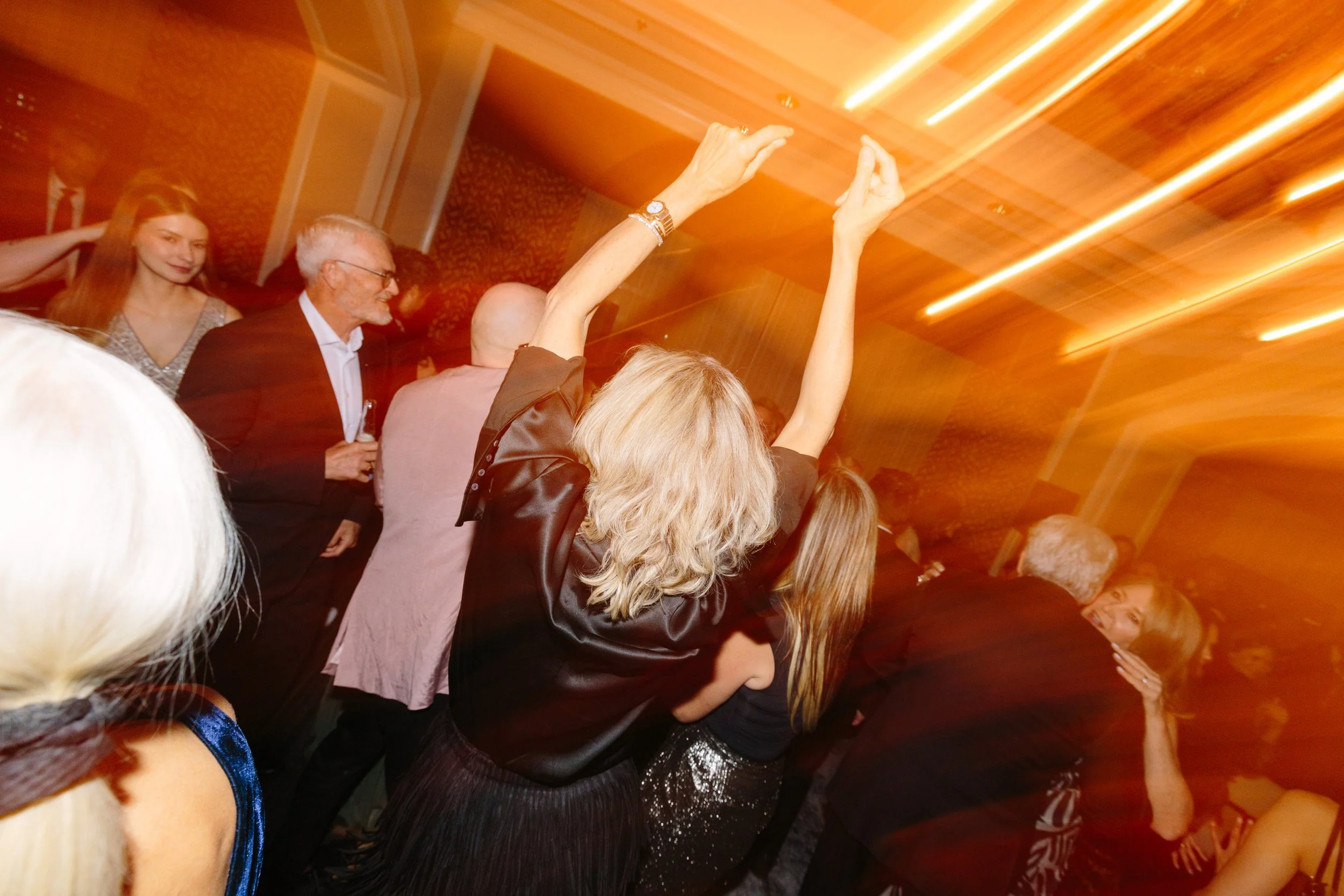 People dancing and celebrating at a lively party with warm lighting and festive atmosphere.