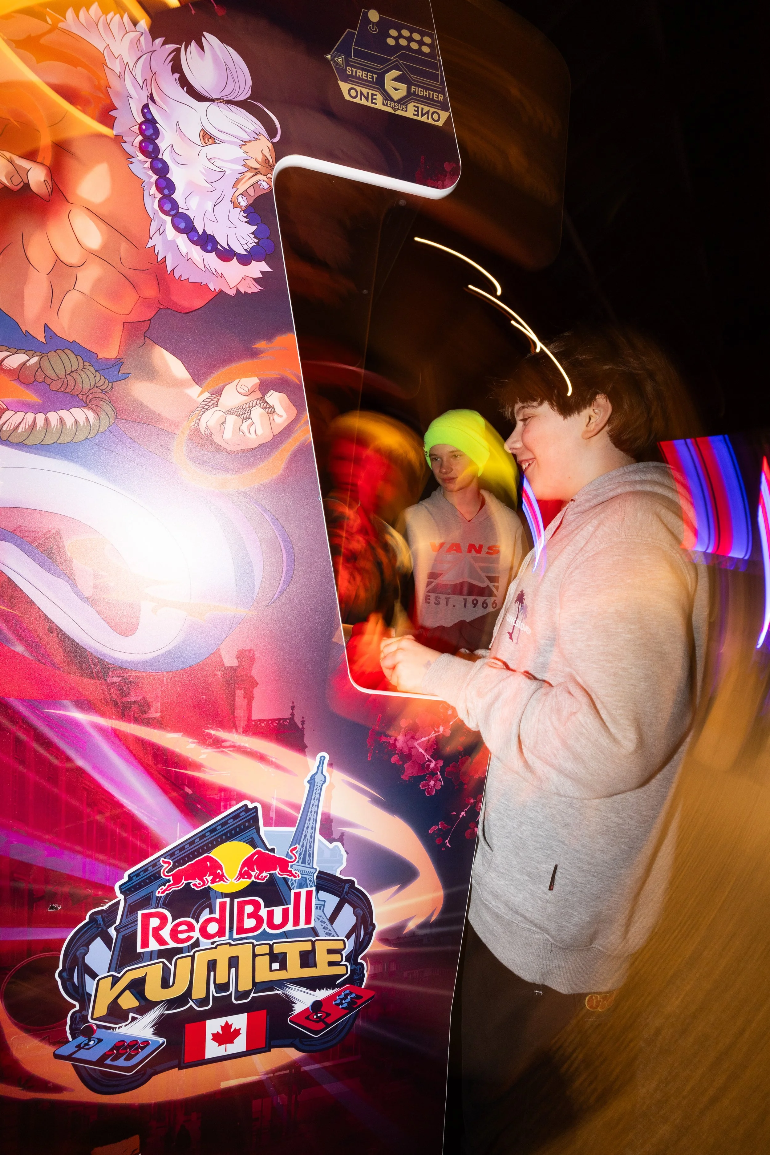 People playing Red Bull Kumite arcade game at an arcade, featuring a colorful dragon illustration and the Red Bull Kumite logo with a Canadian flag.