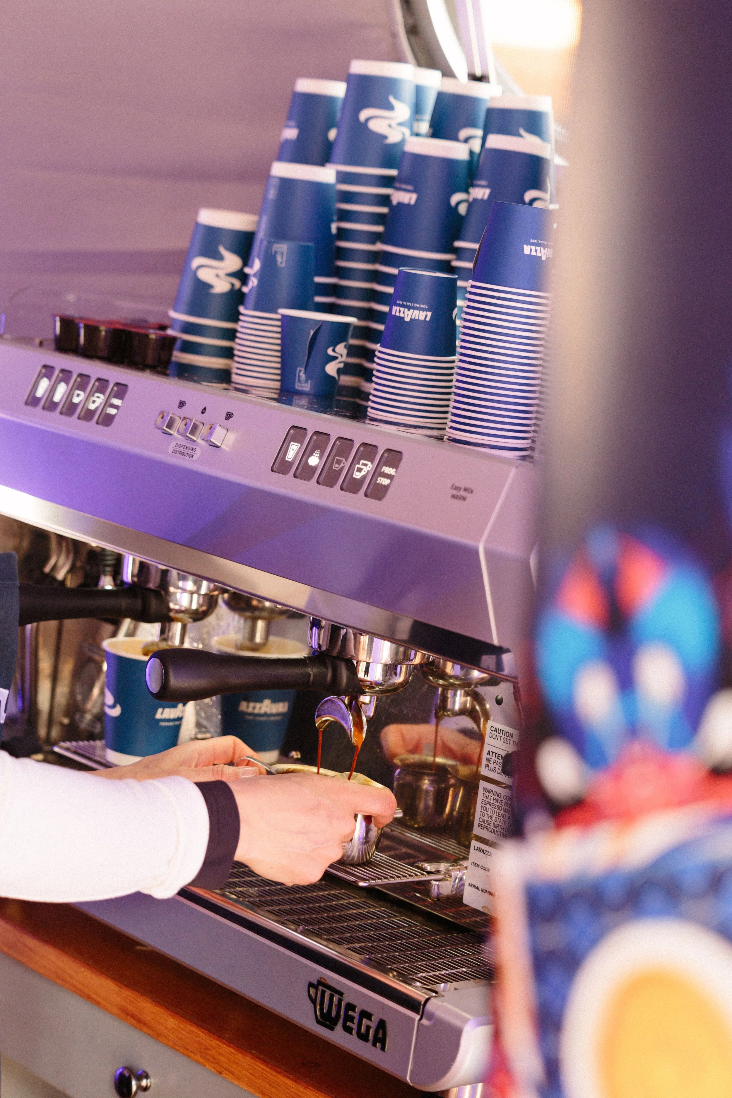 A barista is pouring espresso shots from a coffee machine into a cup held by a customer at a coffee shop or cafe.