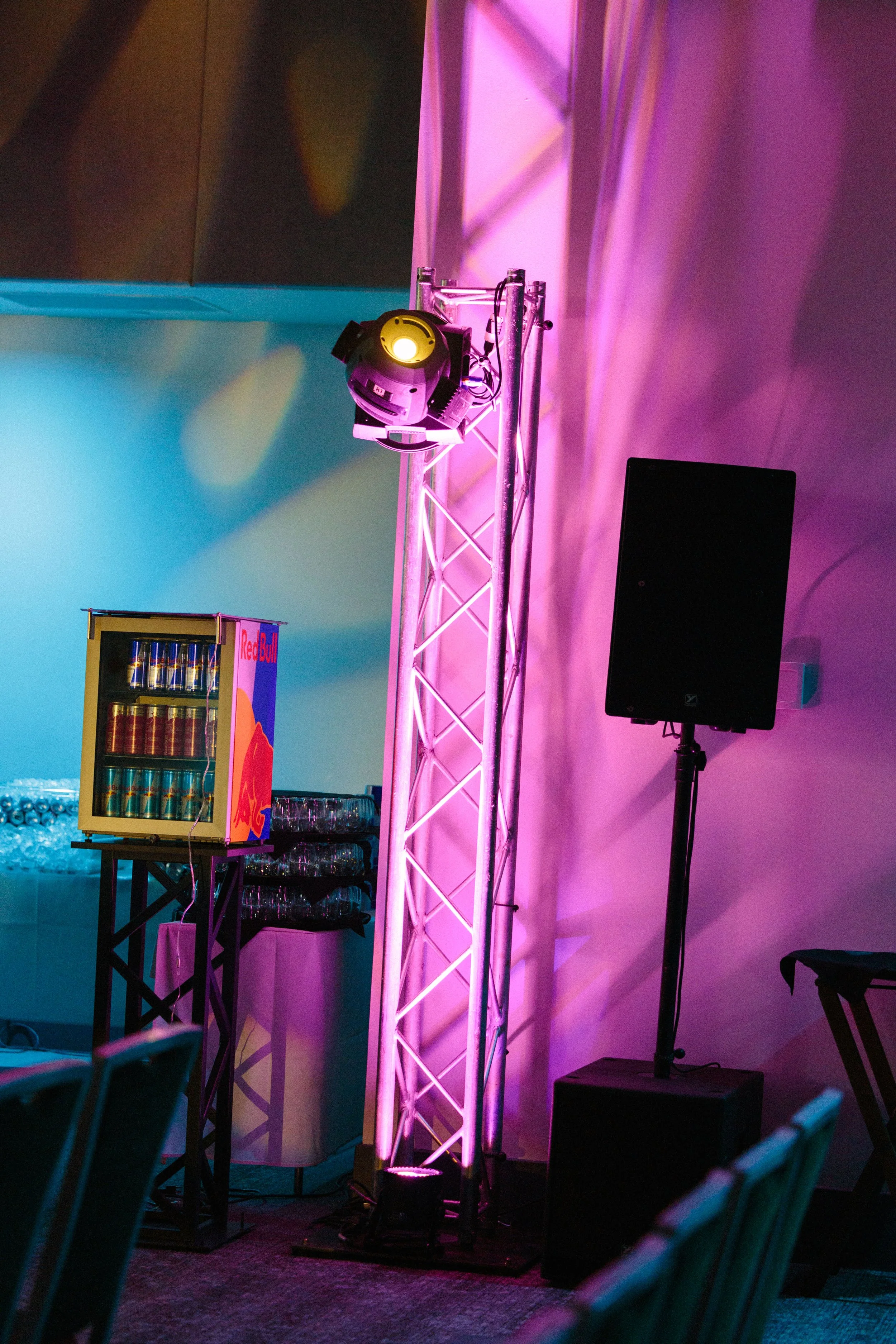 Stage setup with a pink lighting truss, a spotlight on a stand, a black speaker, and a Red Bull display in the background, likely at an event or festival.