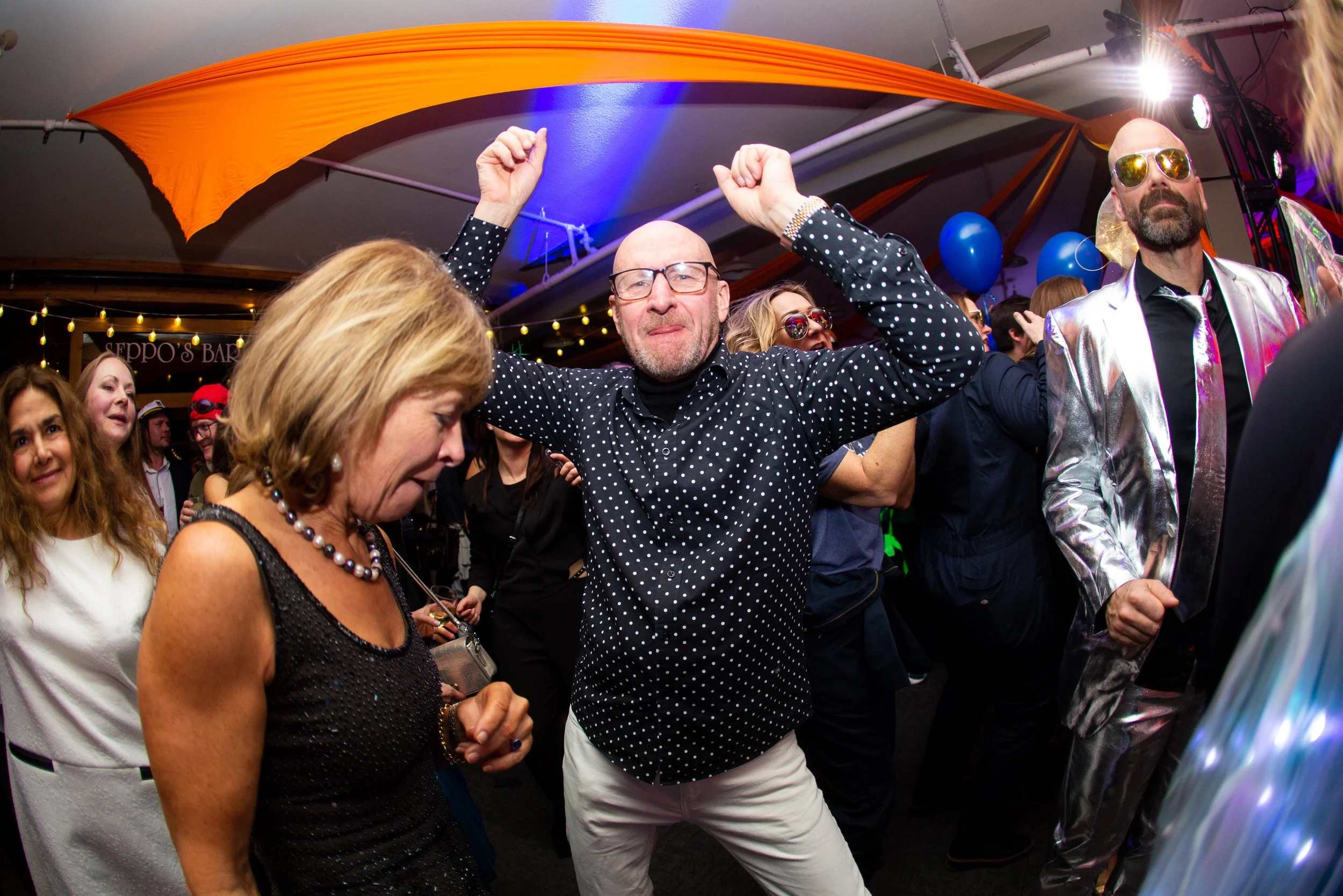 People dancing and celebrating at a lively party or nightclub, with colorful lighting and festive decorations.