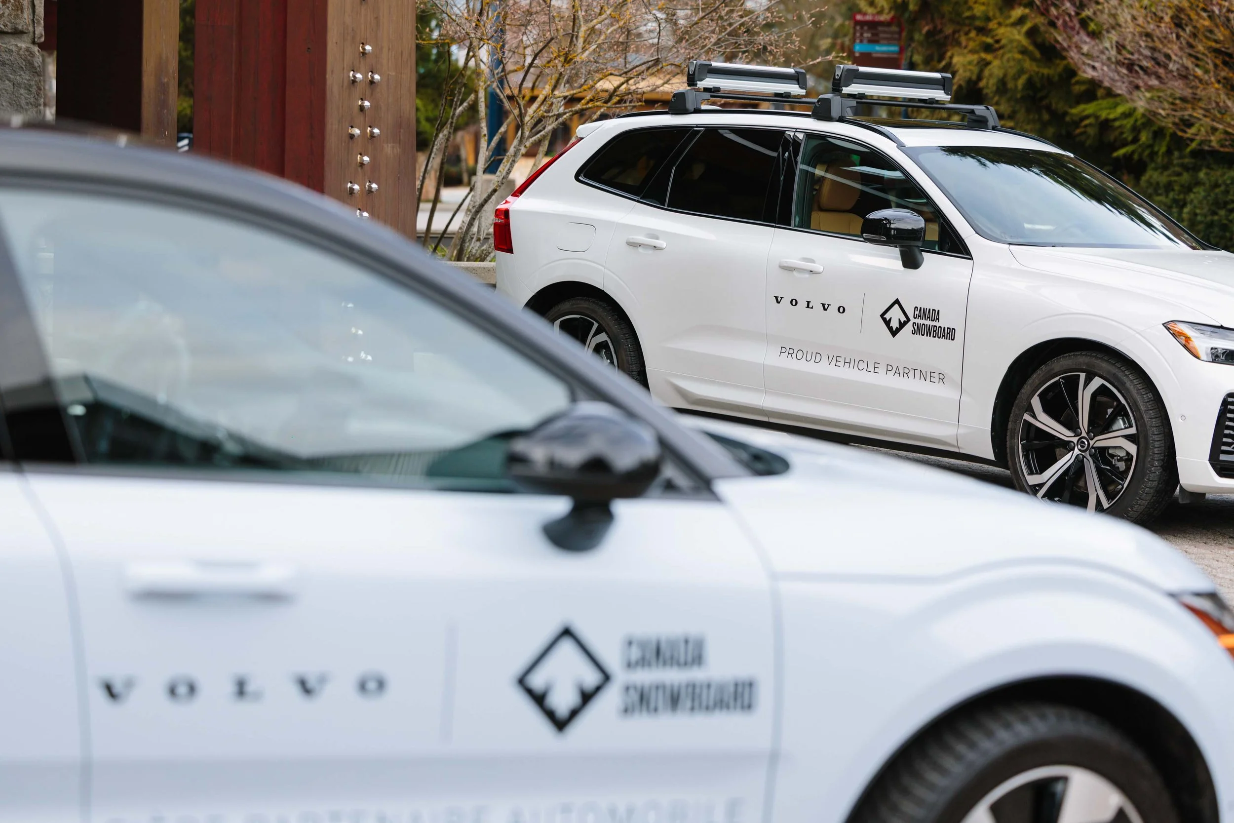 Two white Volvo vehicles parked outdoors, both displaying the Canada Snowboard logo and slogan 'Proud Vehicle Partner' on their sides.