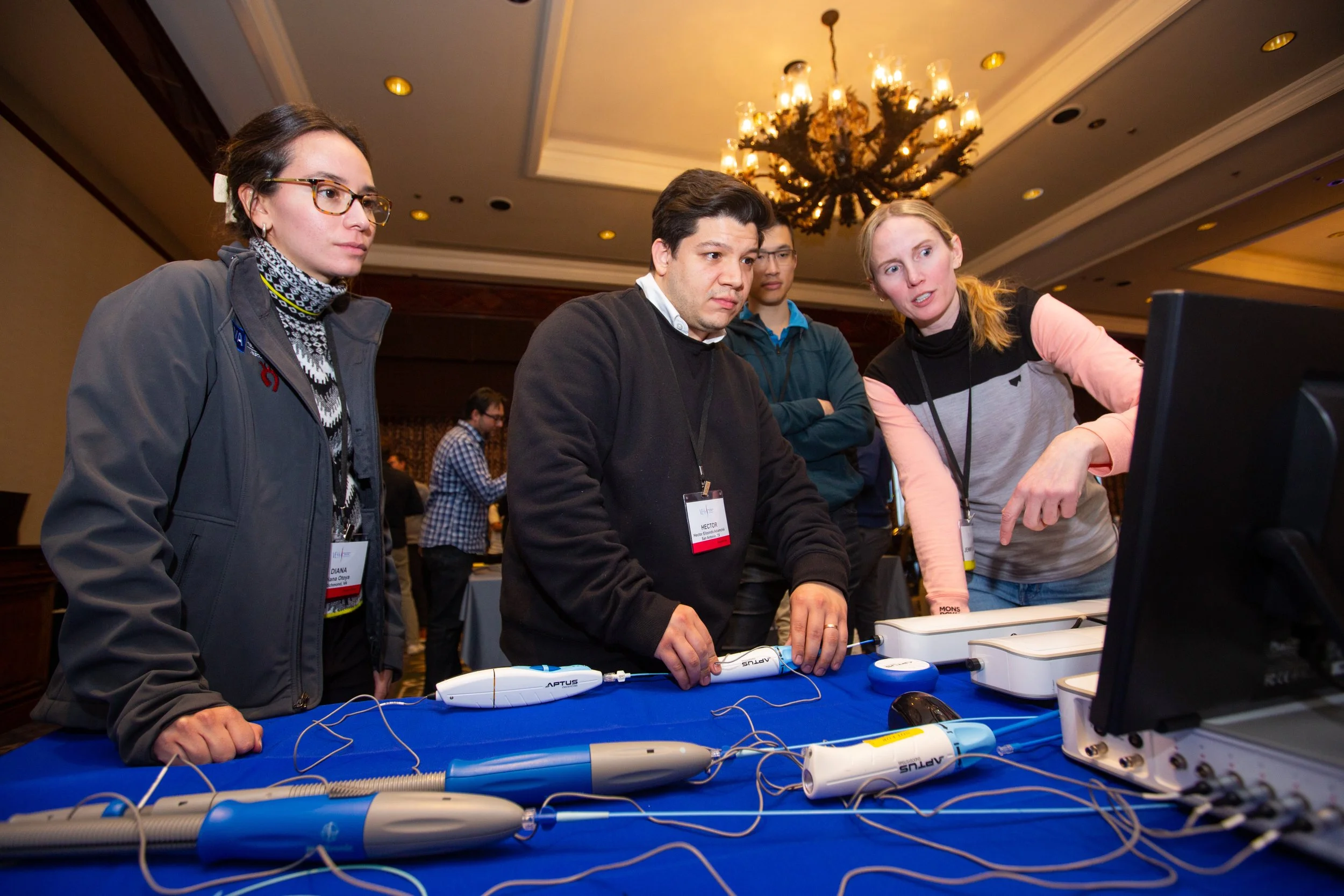 People at a technology demonstration event using medical simulation devices on a table with a computer screen nearby.