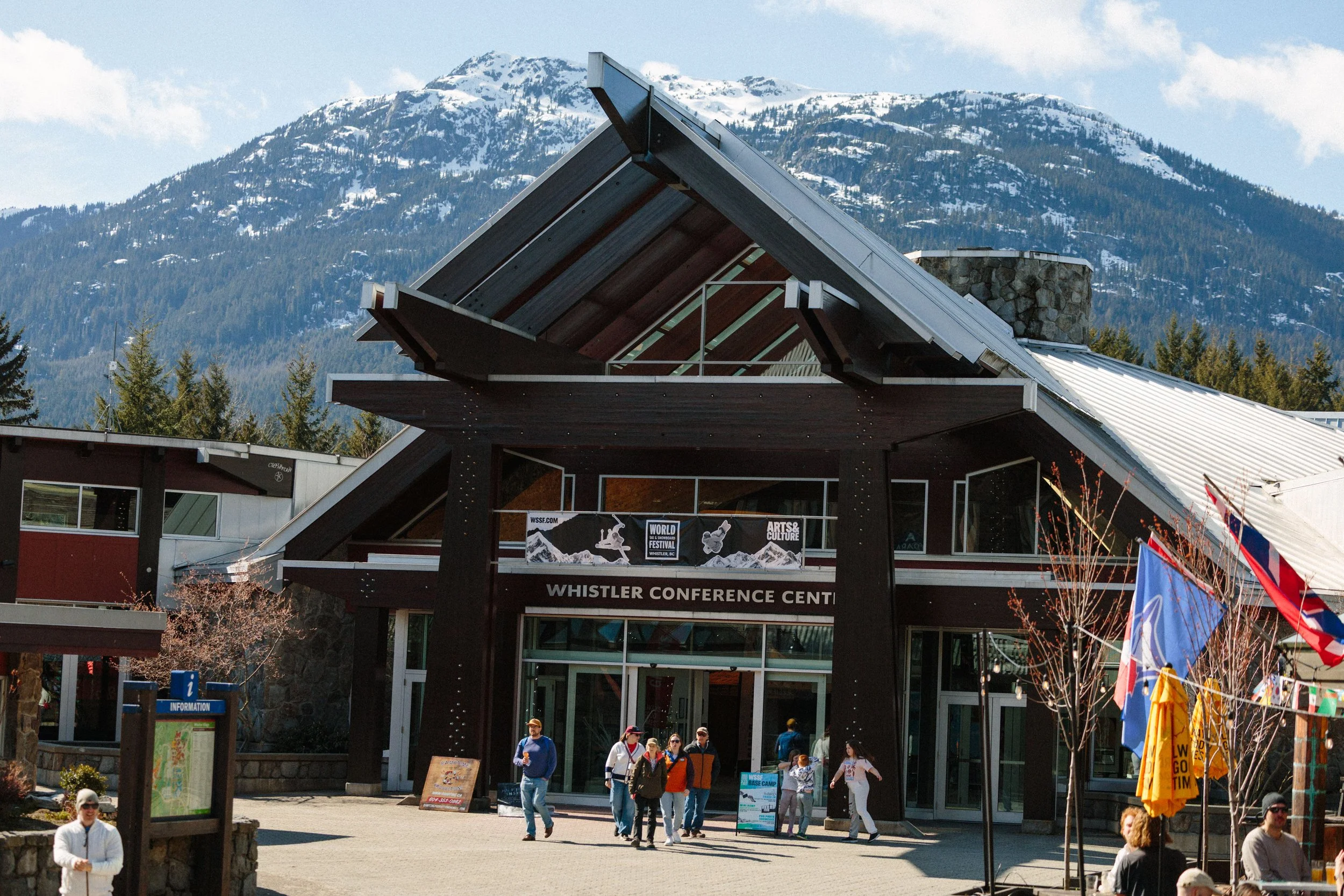 People walking in front of the Whistler Conference Centre with mountains in the background.