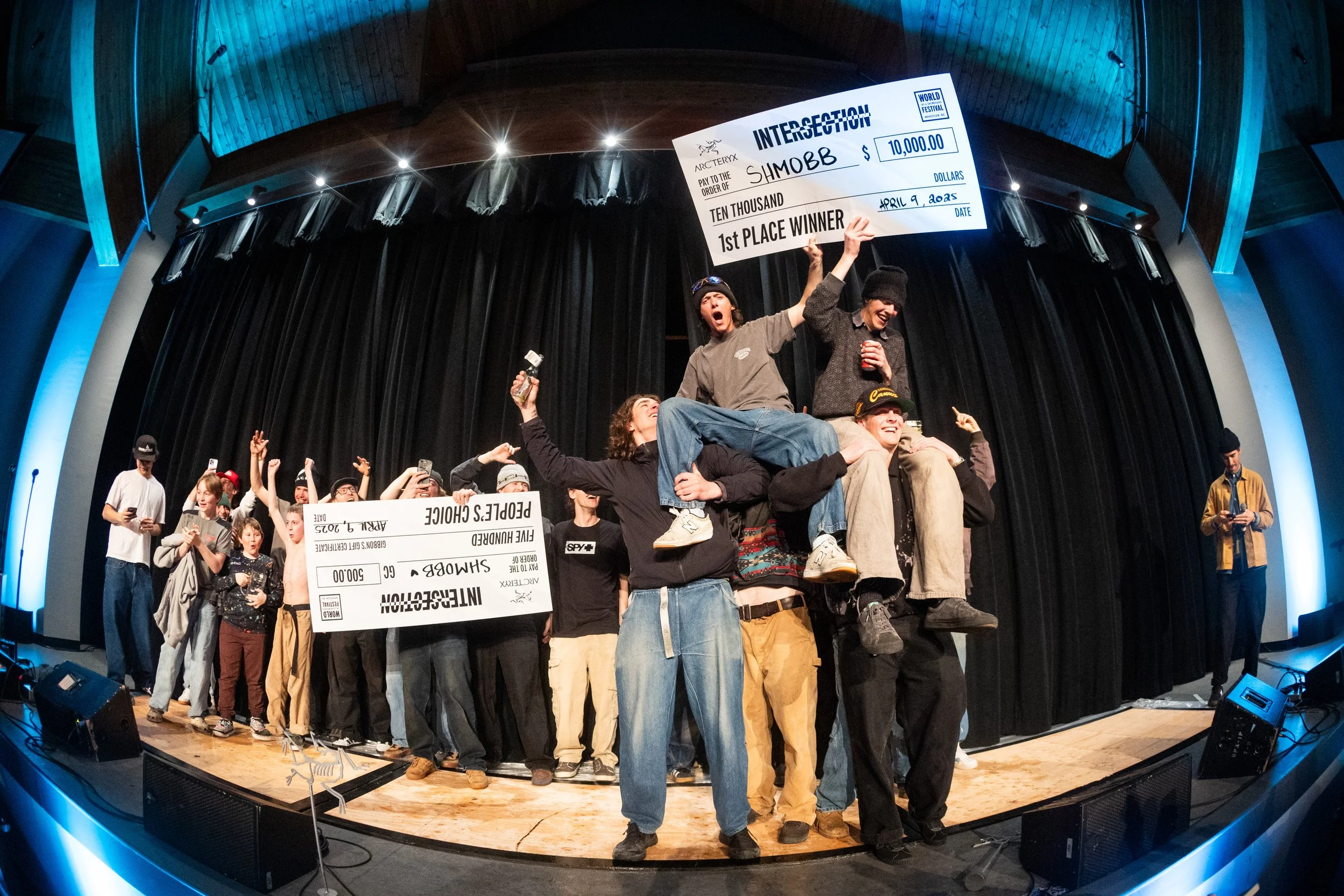Group of people on stage celebrating, holding a large check for $10,000, with some people raising their hands and smiling, during an award or competition event.