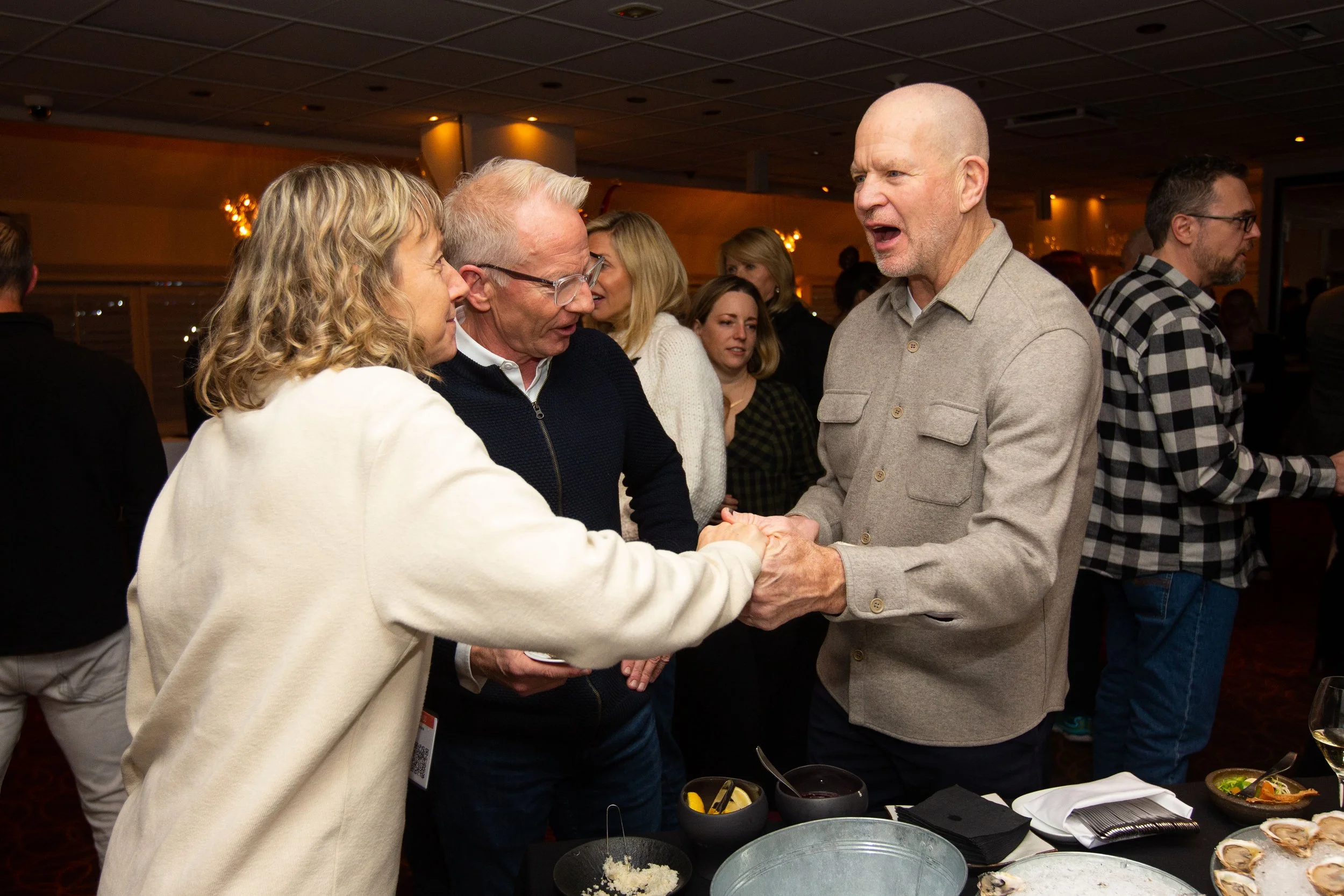 People interacting at a social event in a restaurant setting, with food and drinks on a table.