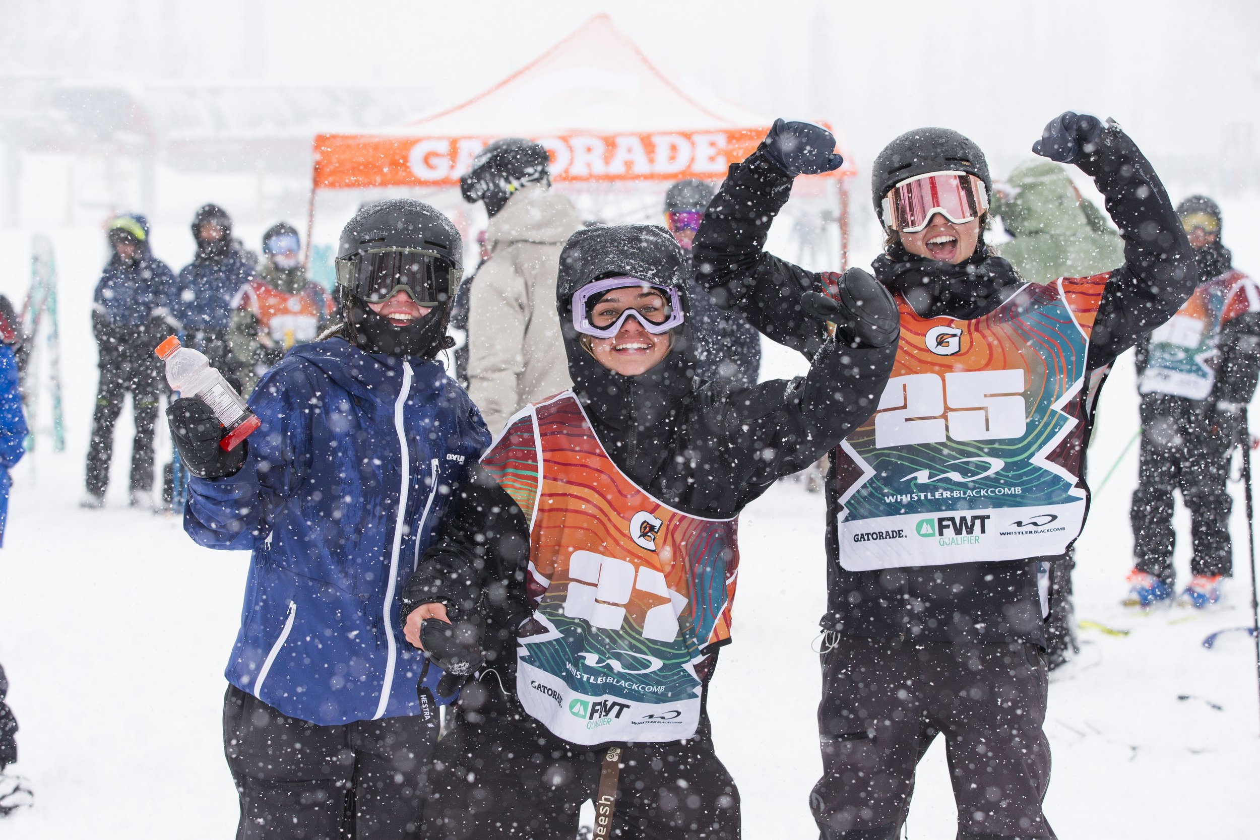 Three young snowboarders celebrating at a snowy ski resort, wearing helmets, goggles, and snow gear, with medals around their necks and a Gatorade tent in the background.