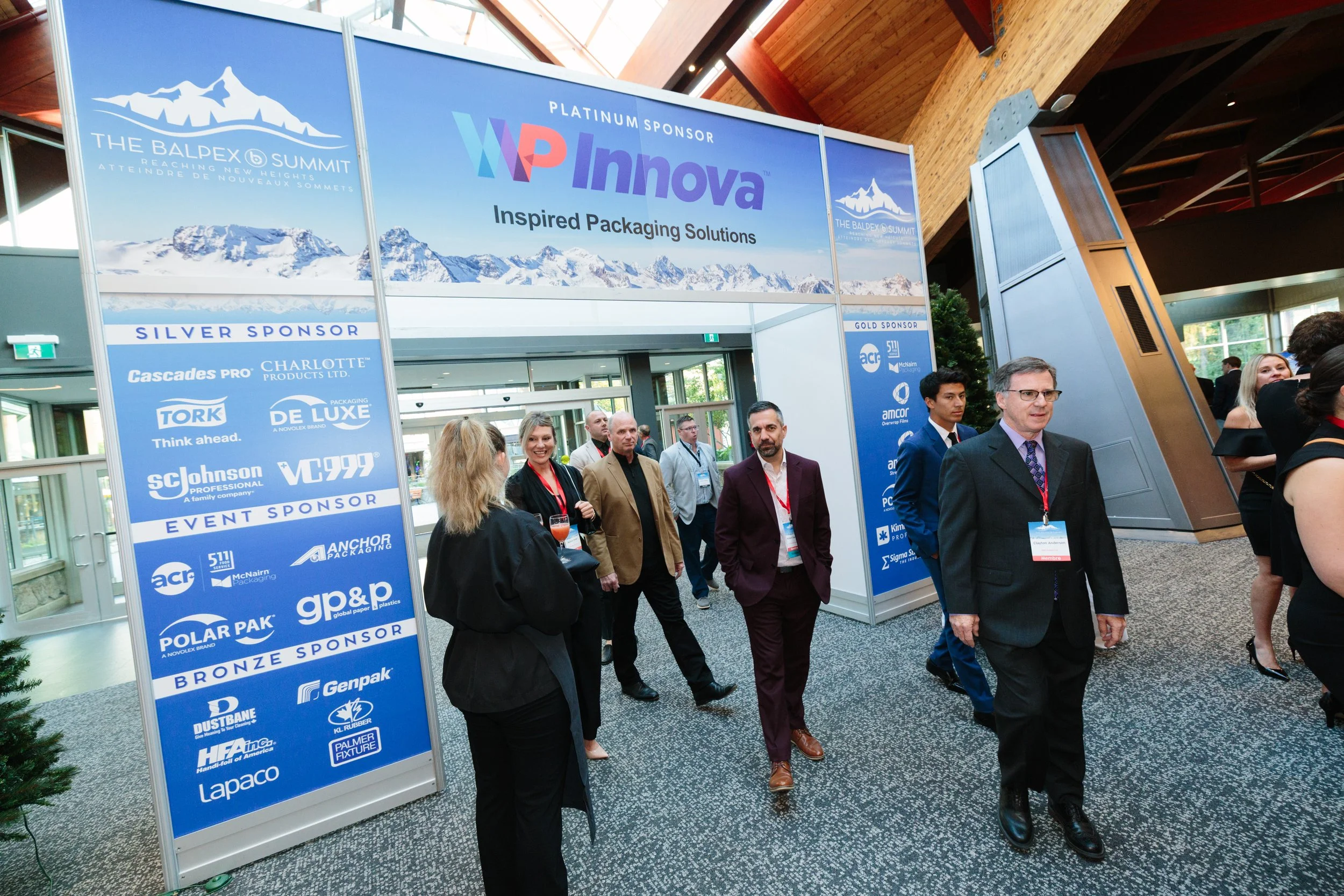 People walking through an indoor conference entrance with sponsor banners displayed overhead and on the sides.