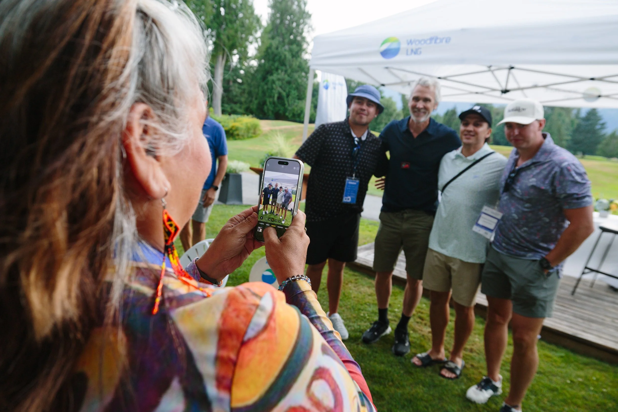 A woman is taking a photo of four men standing under a white tent at an outdoor event.