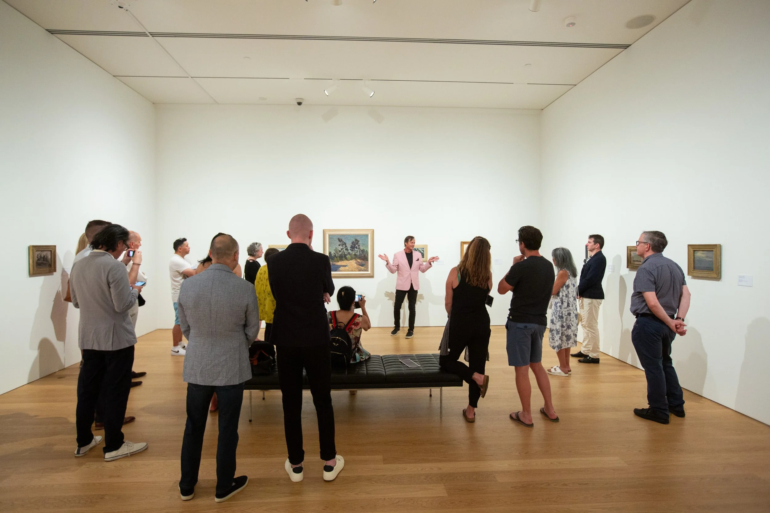 Museum visitor guide giving a talk to a group, with artwork on the white walls behind them.