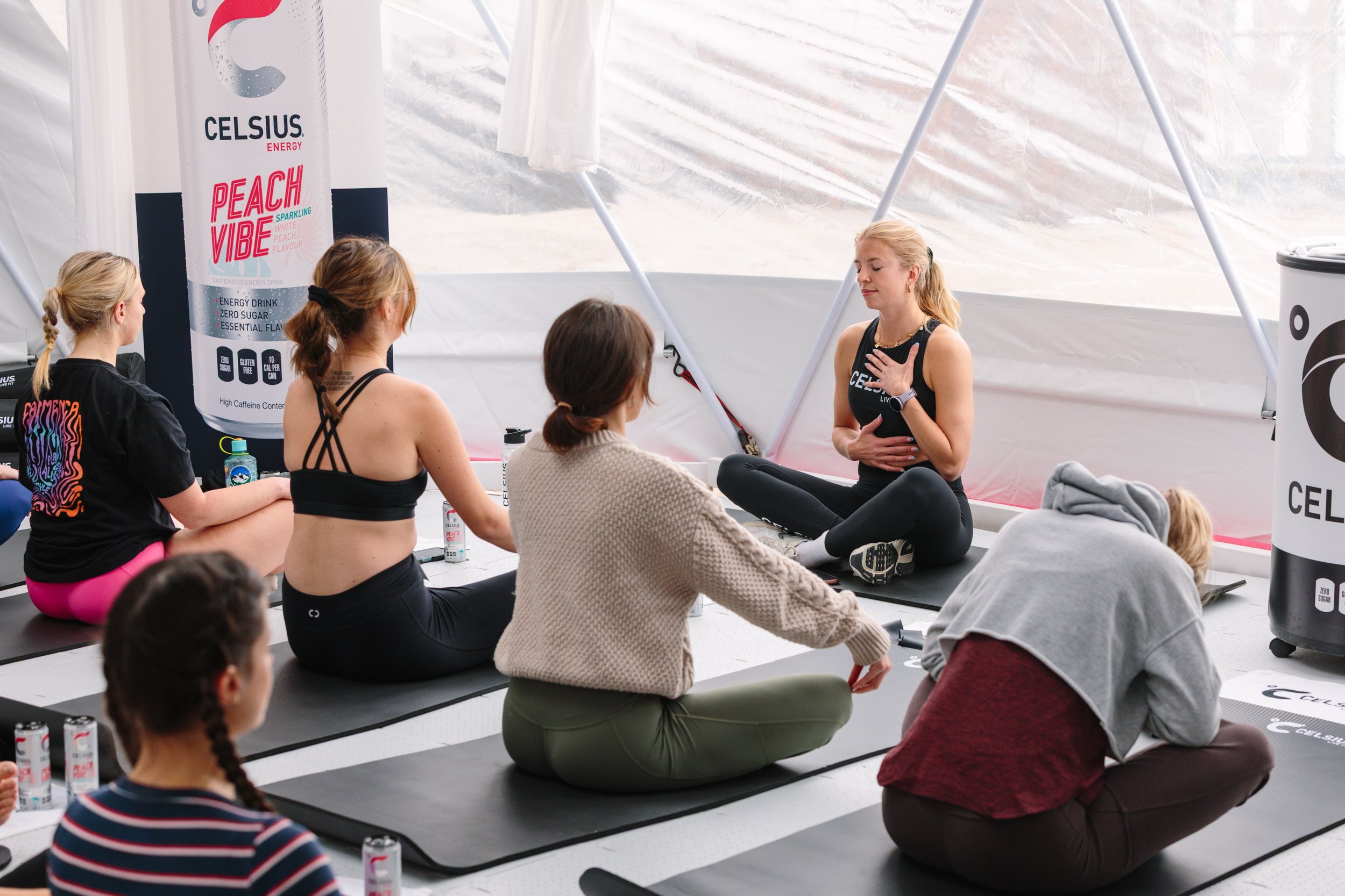 Women participating in a meditation class inside a tent, sitting on yoga mats, with an instructor leading the session.