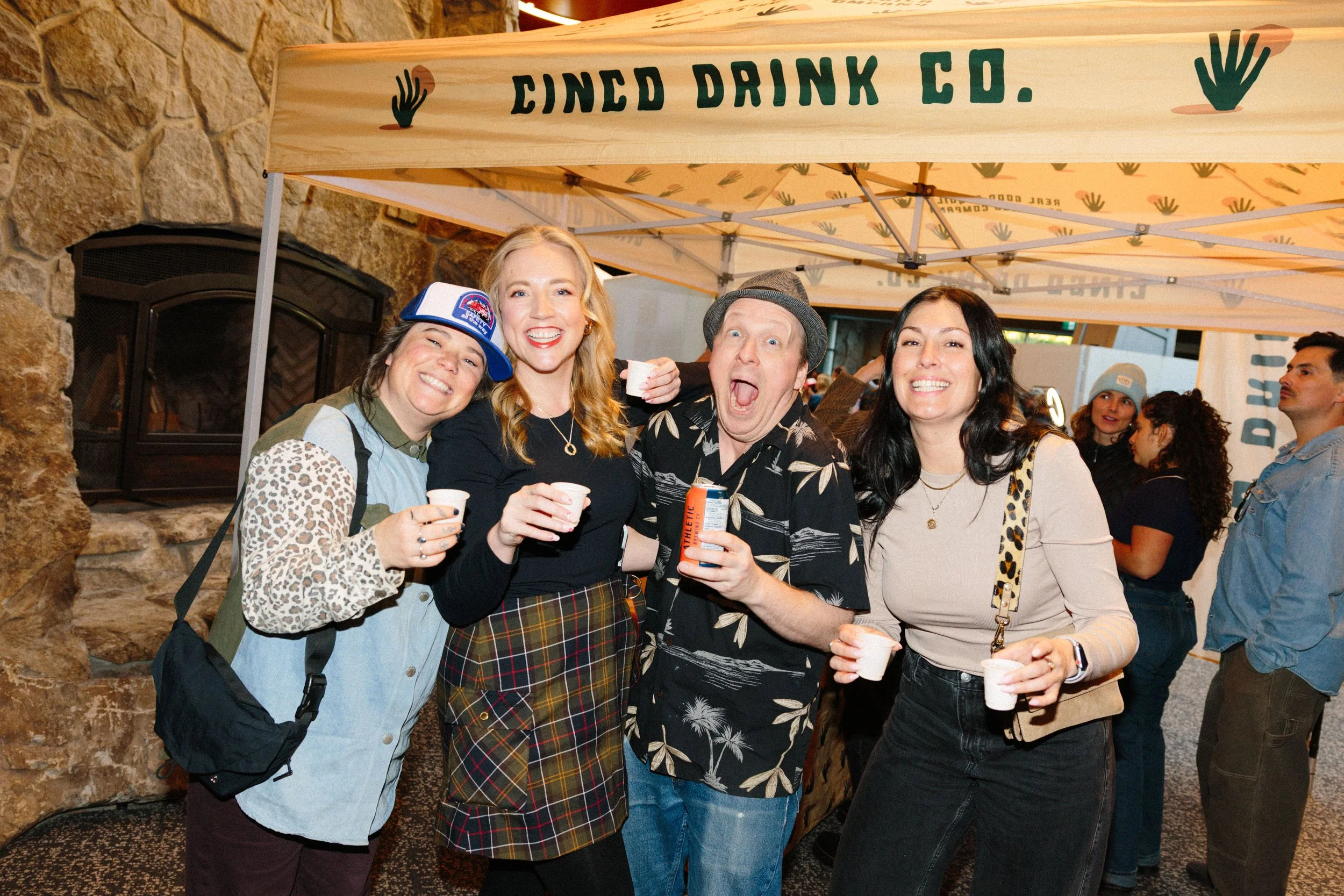 A group of five people smiling and posing at an indoor event, with the sign 'Cinced Drink Co.' visible above them.