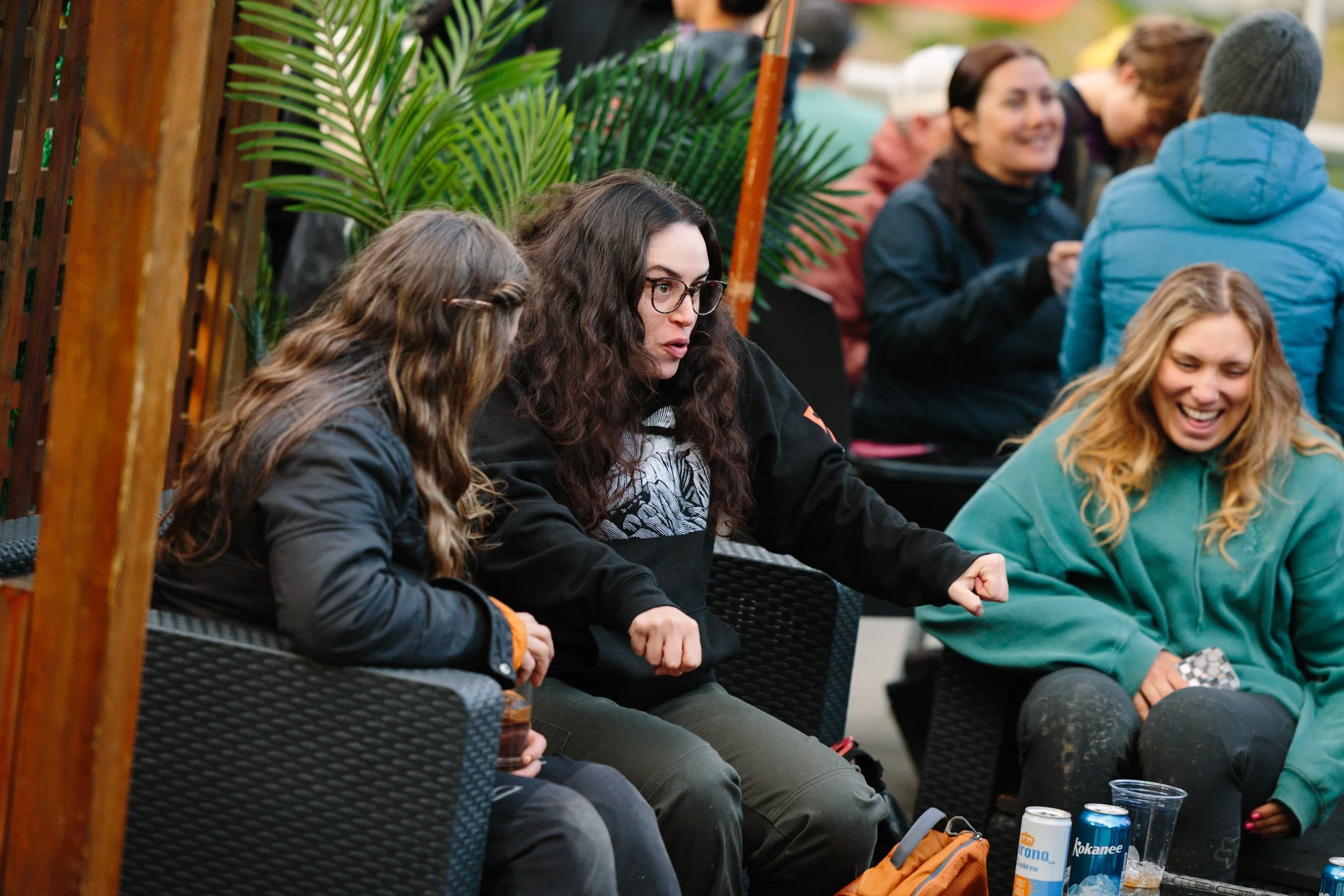 Group of people sitting outdoors, engaging in conversation and laughter, with drinks and beverages on the table in front.
