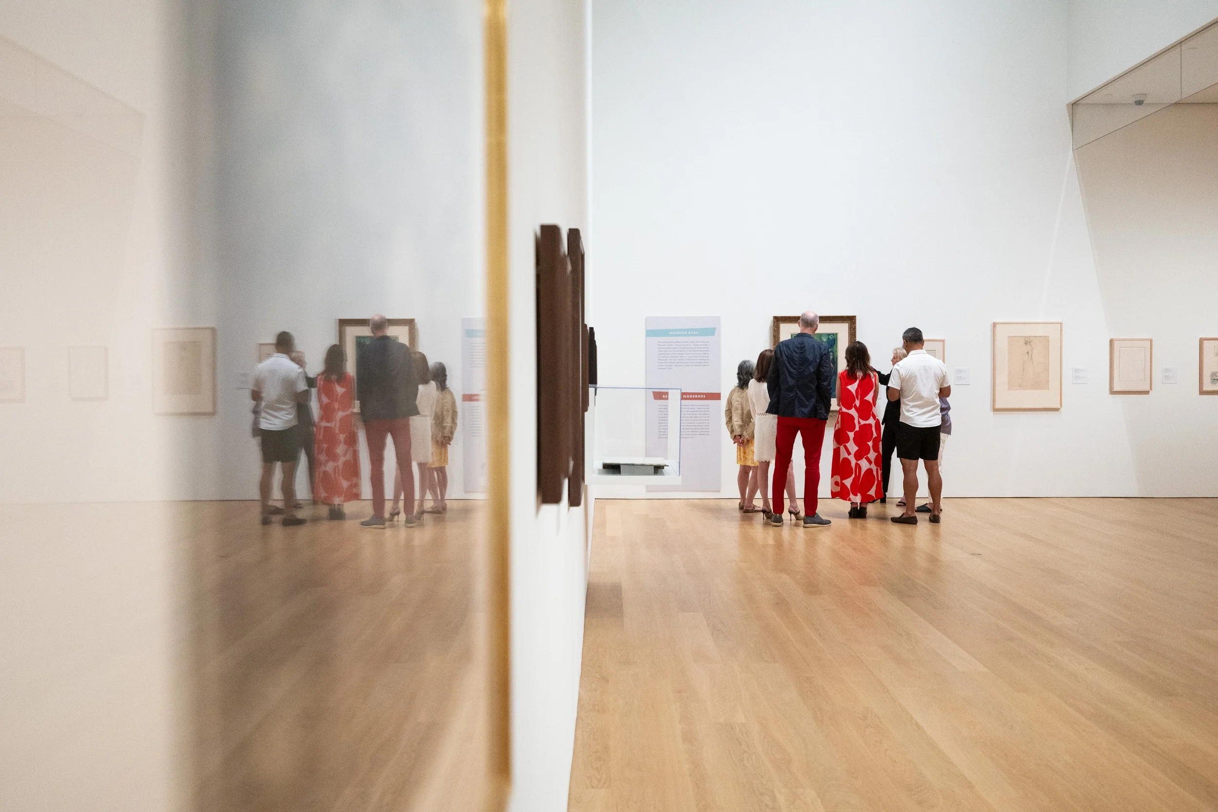 People viewing artwork in a museum, seen through a mirror reflecting the scene.