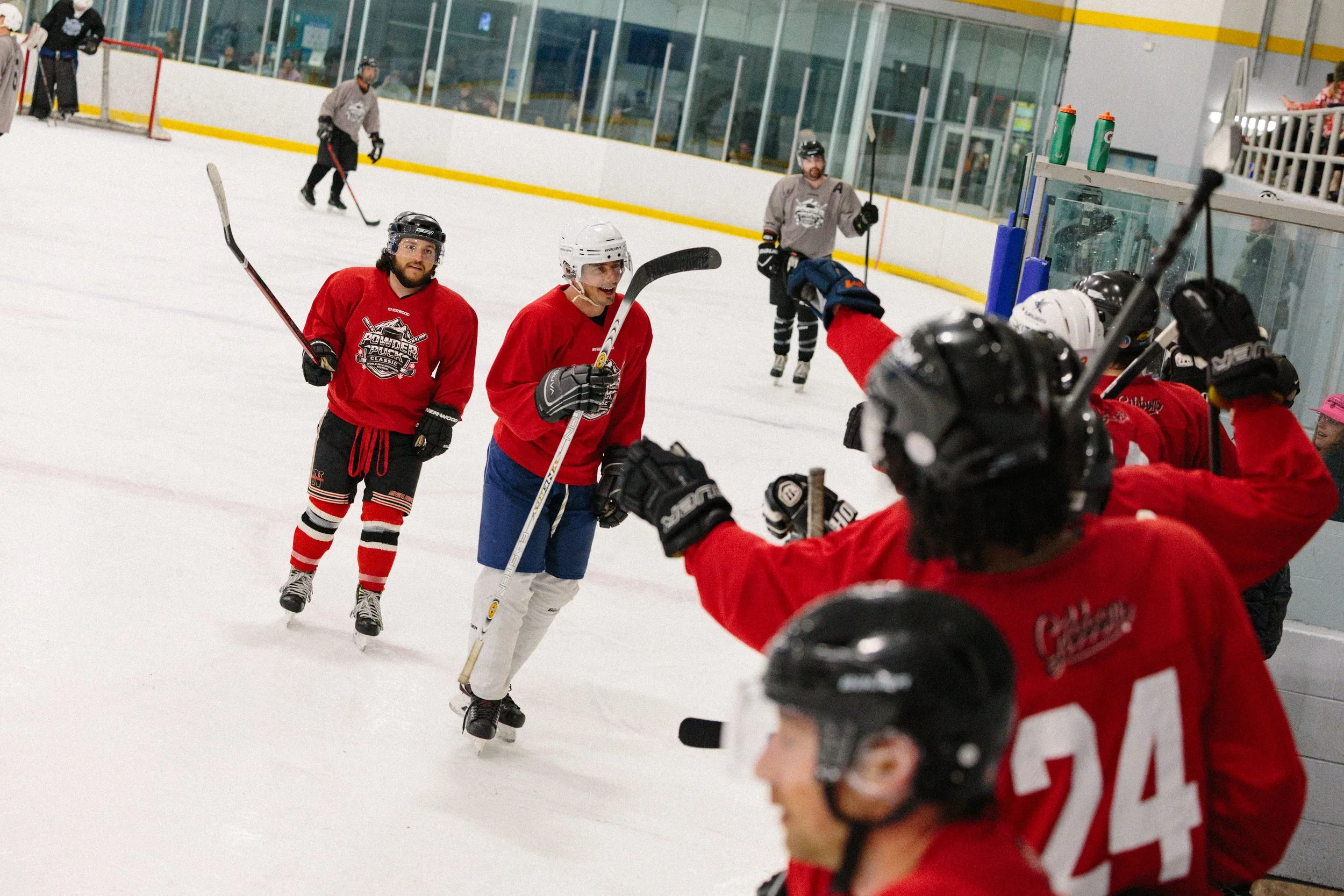 Hockey players on an ice rink celebrating, wearing red jerseys, with some players sitting and others standing, including a player with a white helmet in the center.