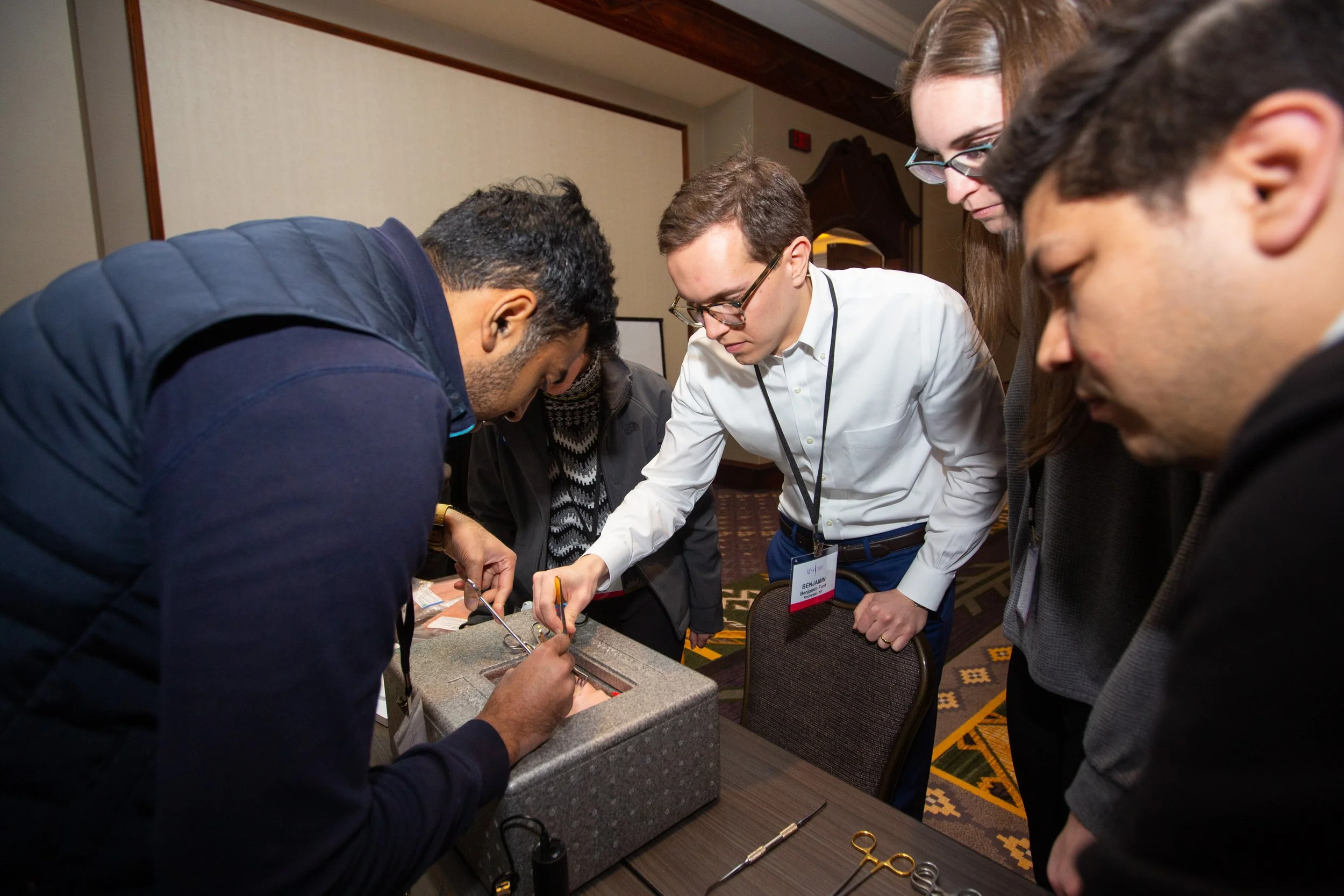 People conducting a medical simulation exercise with surgical instruments, focused on hands-on practice using a foam-like material.