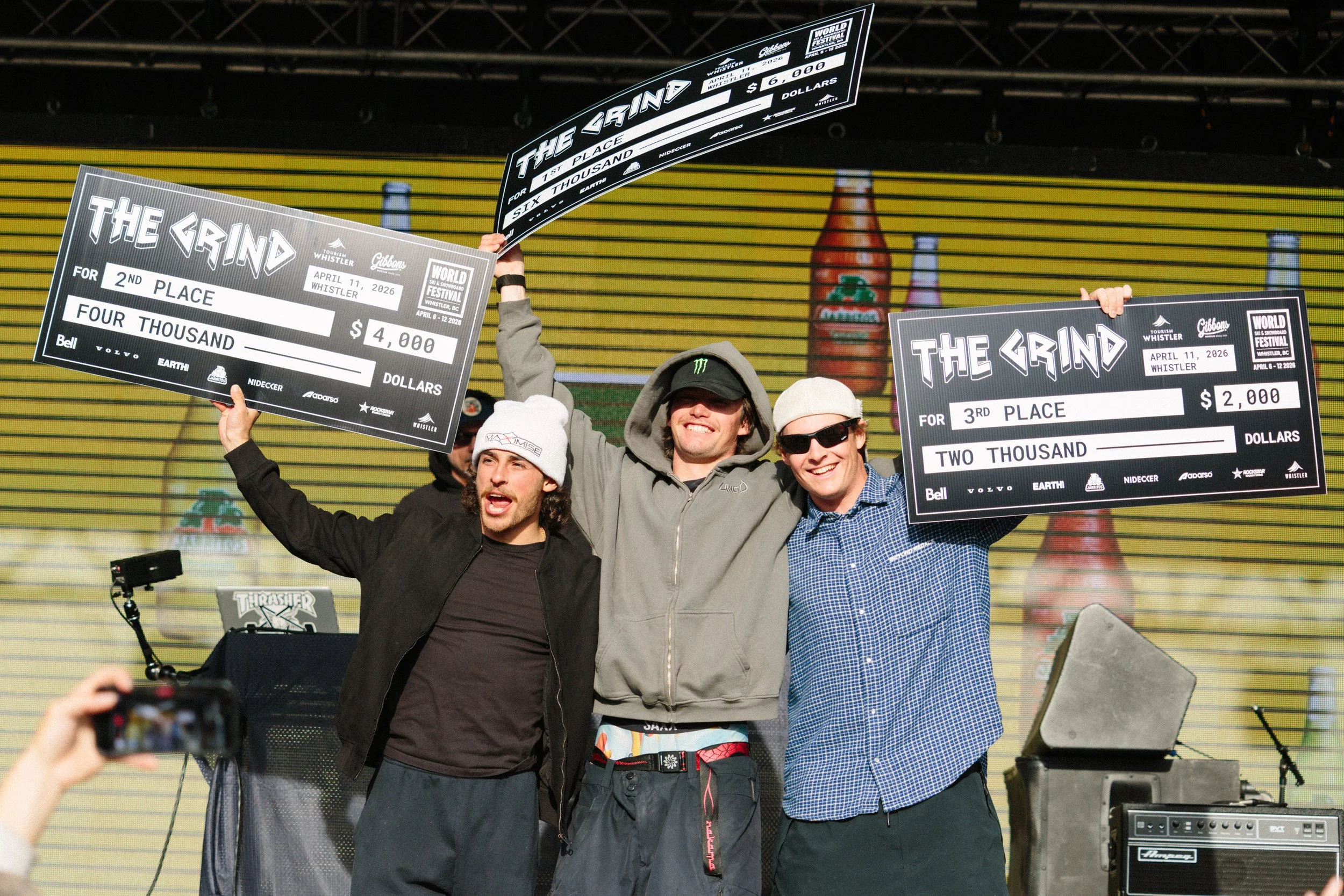 Three men standing on a stage holding large checks, celebrating a competition at the Whistler World Festival on April 11, 2026.